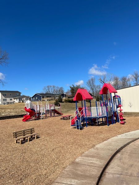Playground with red, blue, and white equipment on wood chips under a clear blue sky.