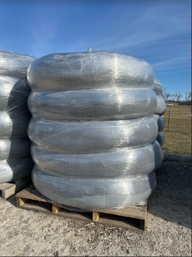 Coils of metal wire wrapped in plastic, stacked on a wooden pallet outdoors.