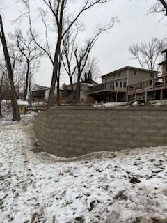 Snowy landscape with a retaining wall, houses, and bare trees.