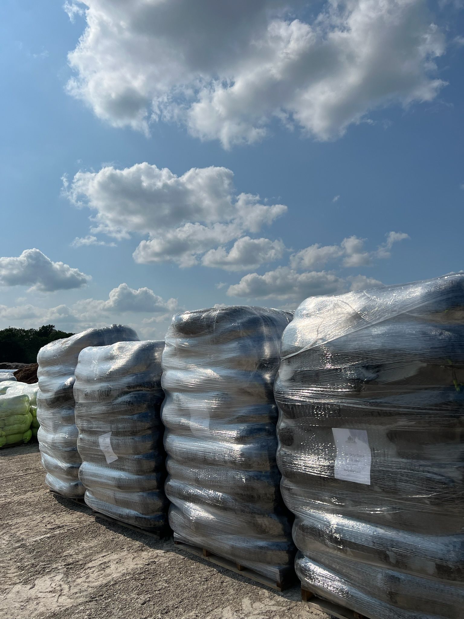 Bales of wrapped material stacked outdoors against a blue sky with fluffy clouds.