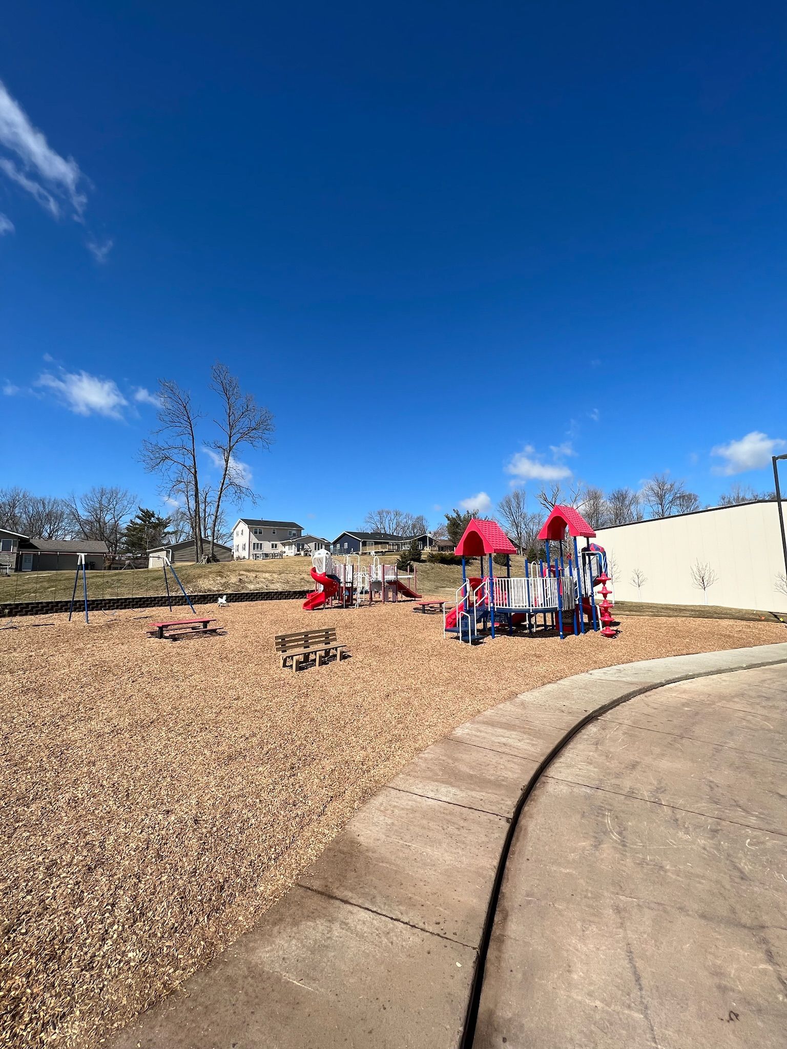 Playground with red and blue equipment on wood chips under a blue sky.