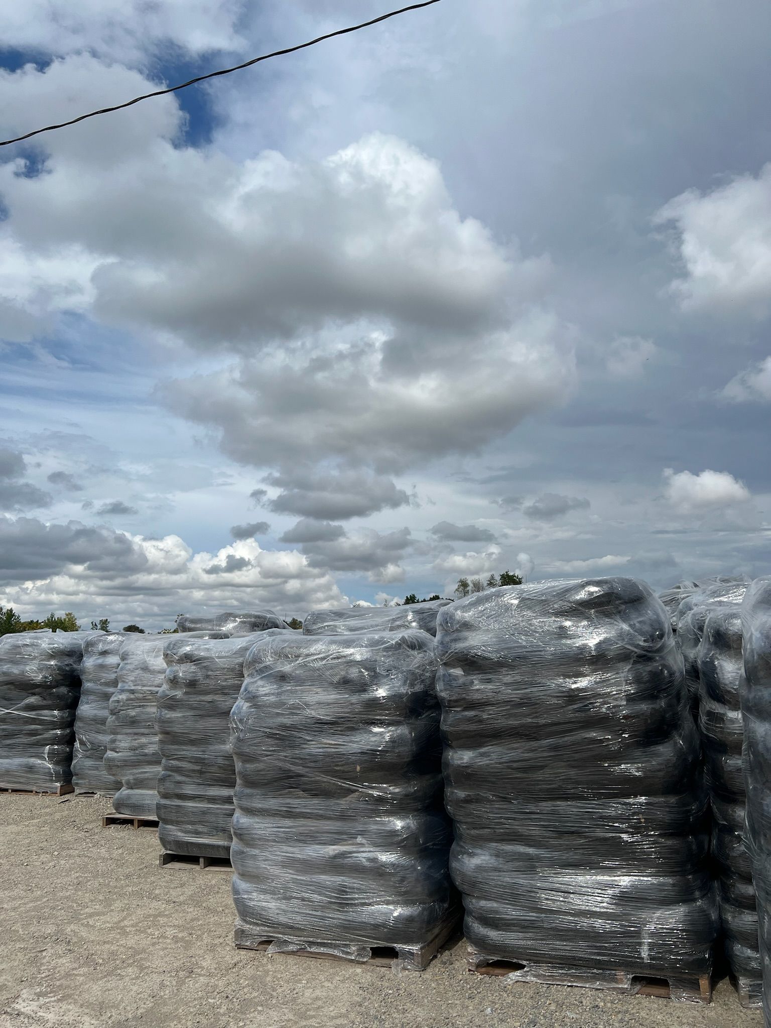 Stacks of wrapped, dark-colored materials on pallets under a cloudy sky.