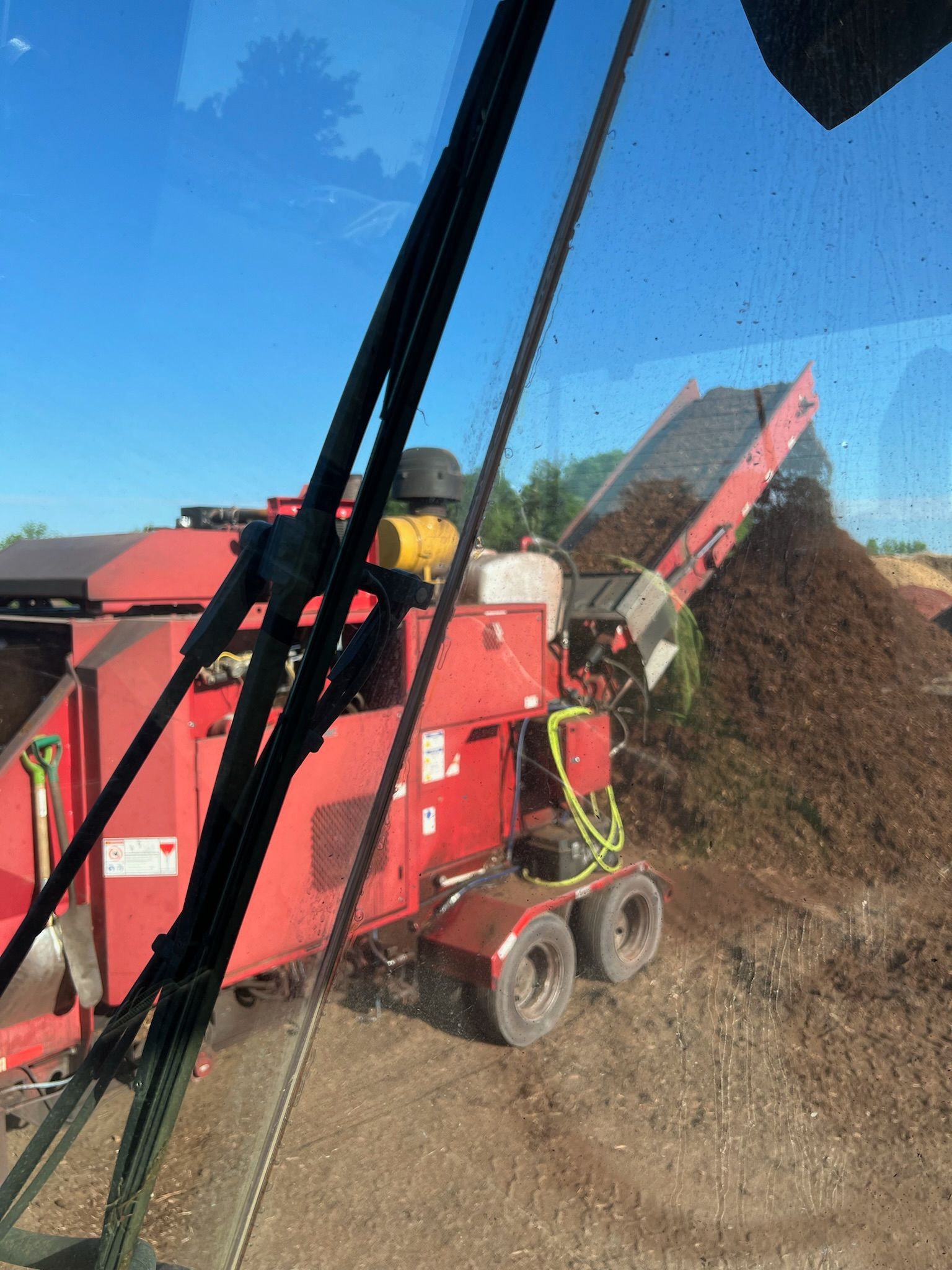 Red machine processing wood chips outdoors, blue sky.