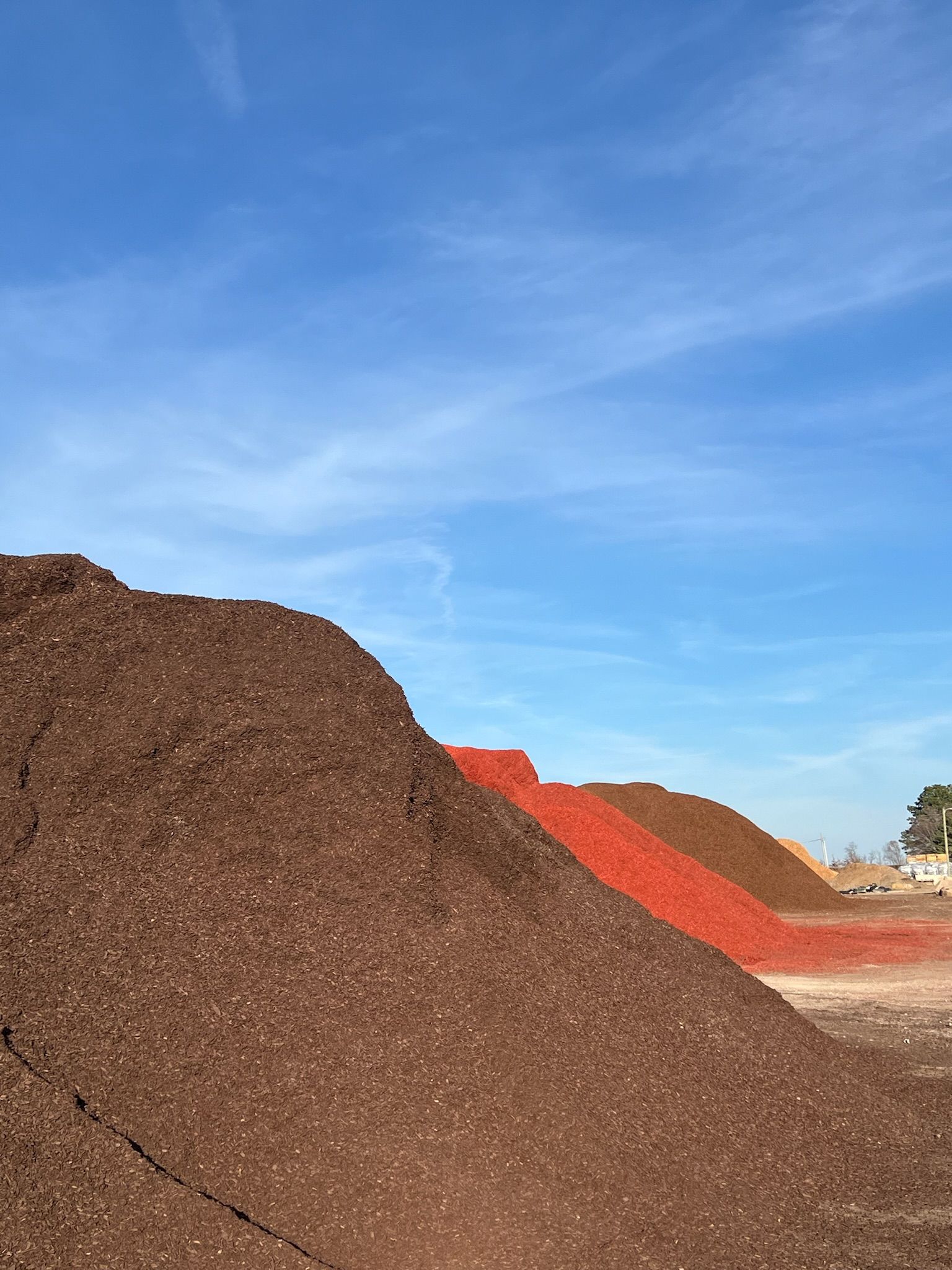 Piles of brown, red, and tan mulch against a bright blue sky.