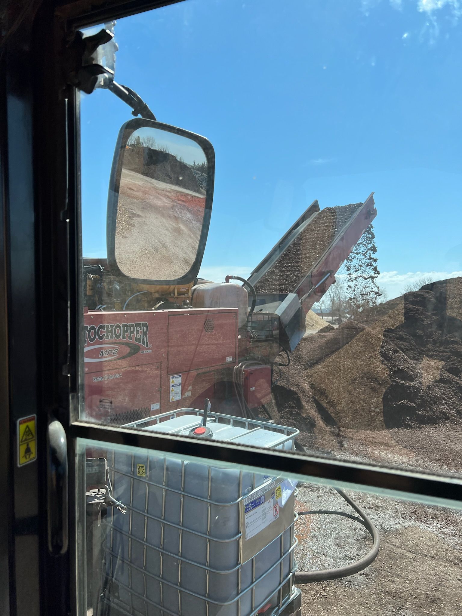 View from inside cab of wood chipper, with wood being dumped on a pile.