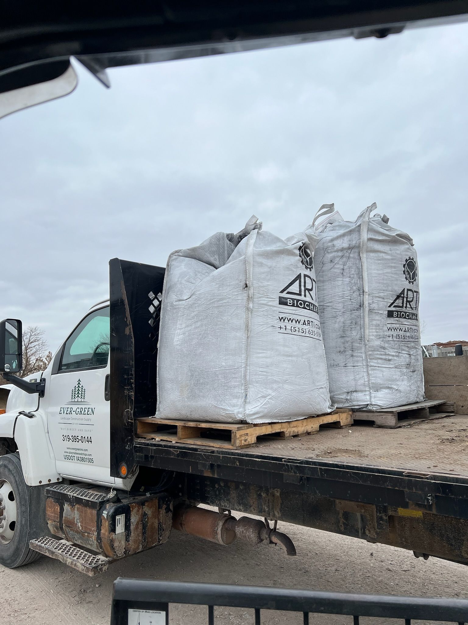 Two large bags of material on pallets in the bed of a white flatbed truck.