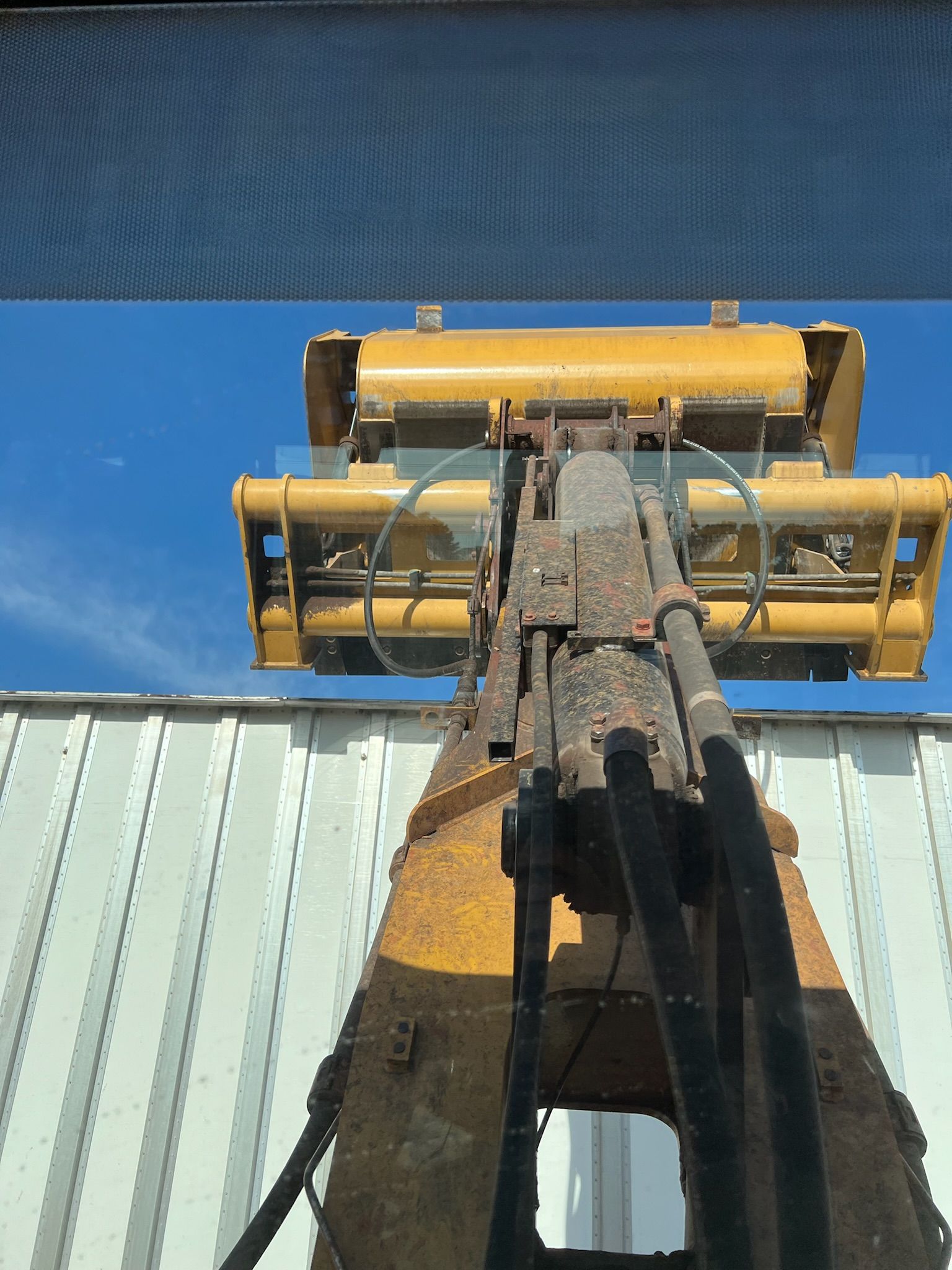 Yellow forklift lifting a container, seen from below, against a blue sky.