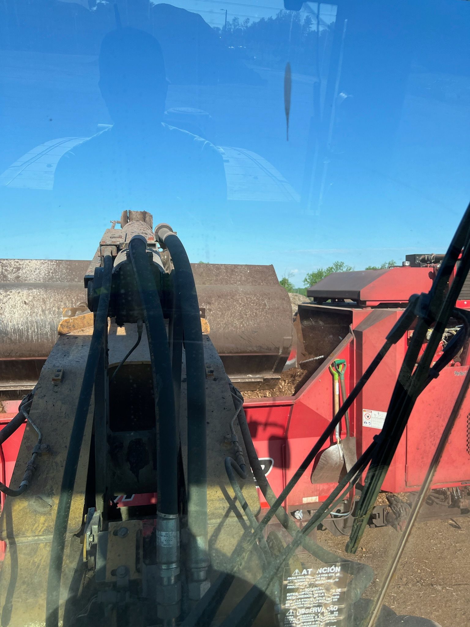 View from inside a machine with red and black parts; a building and blue sky seen through glass.