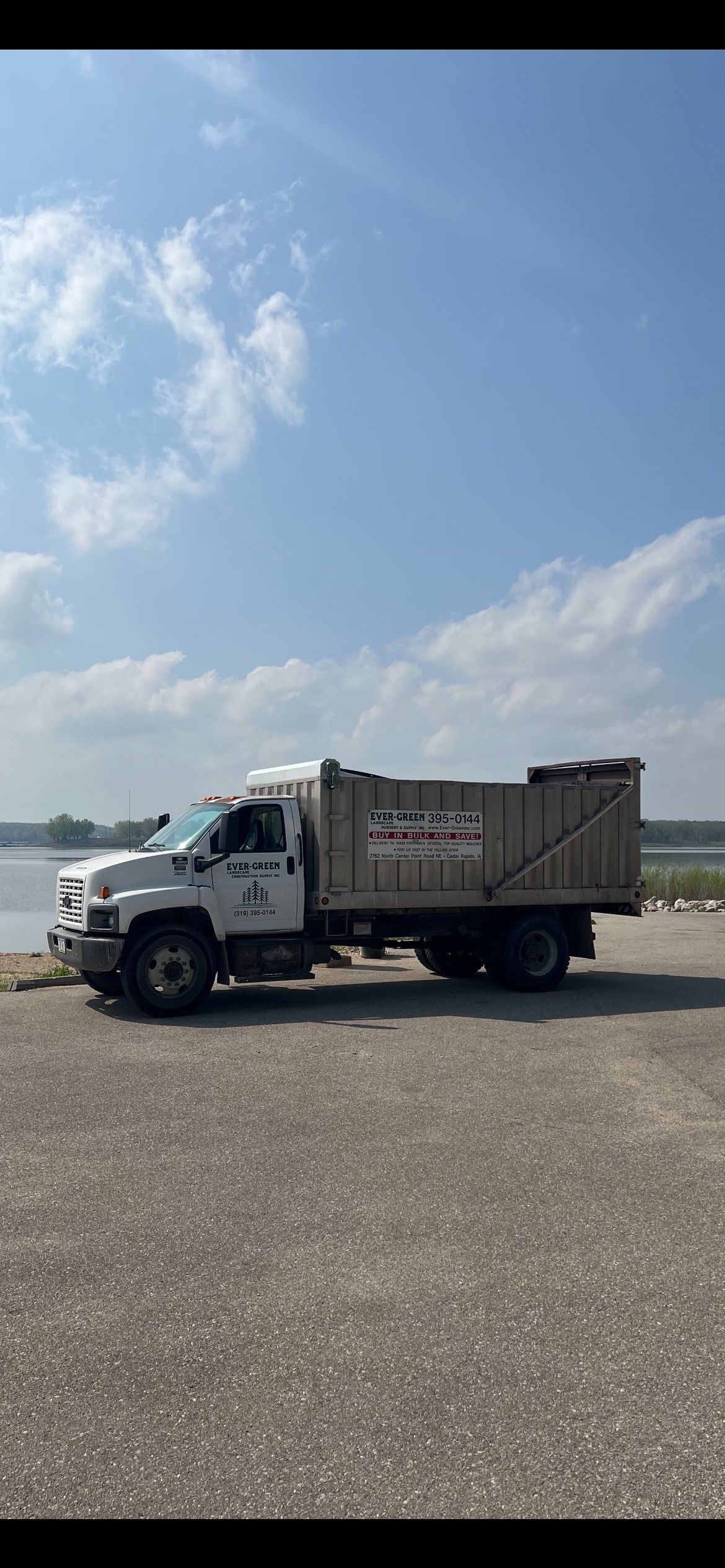 White dump truck parked on gravel near water under a blue sky.