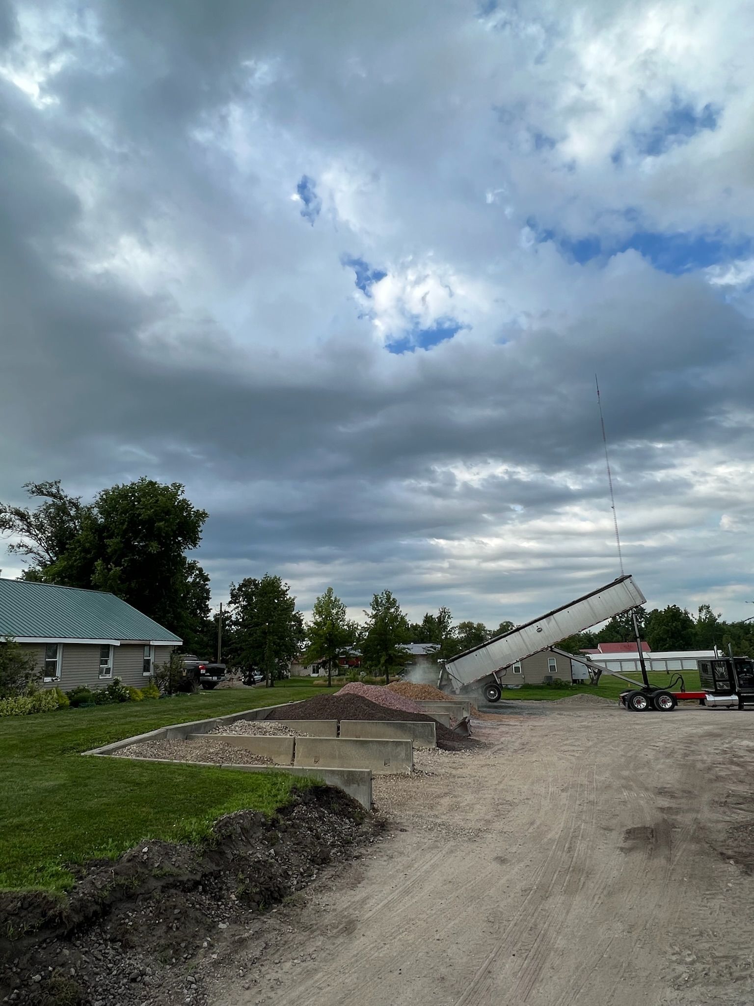 Truck unloading material onto a construction site with a cloudy sky overhead.