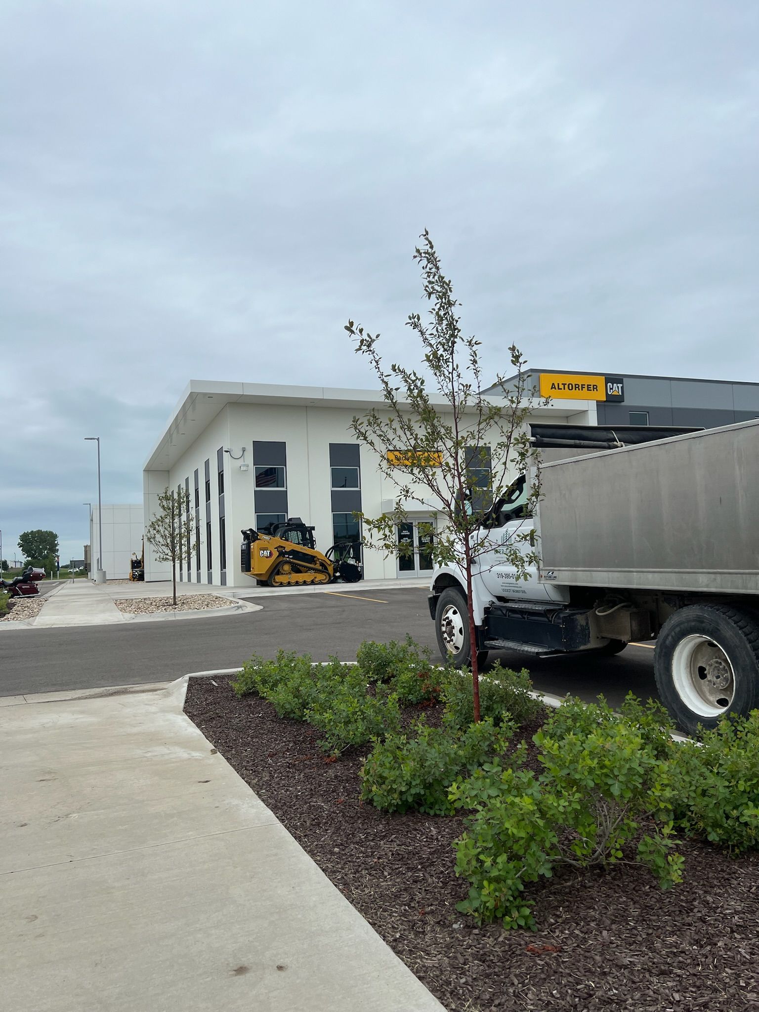 White building with construction equipment, truck, and landscaping.