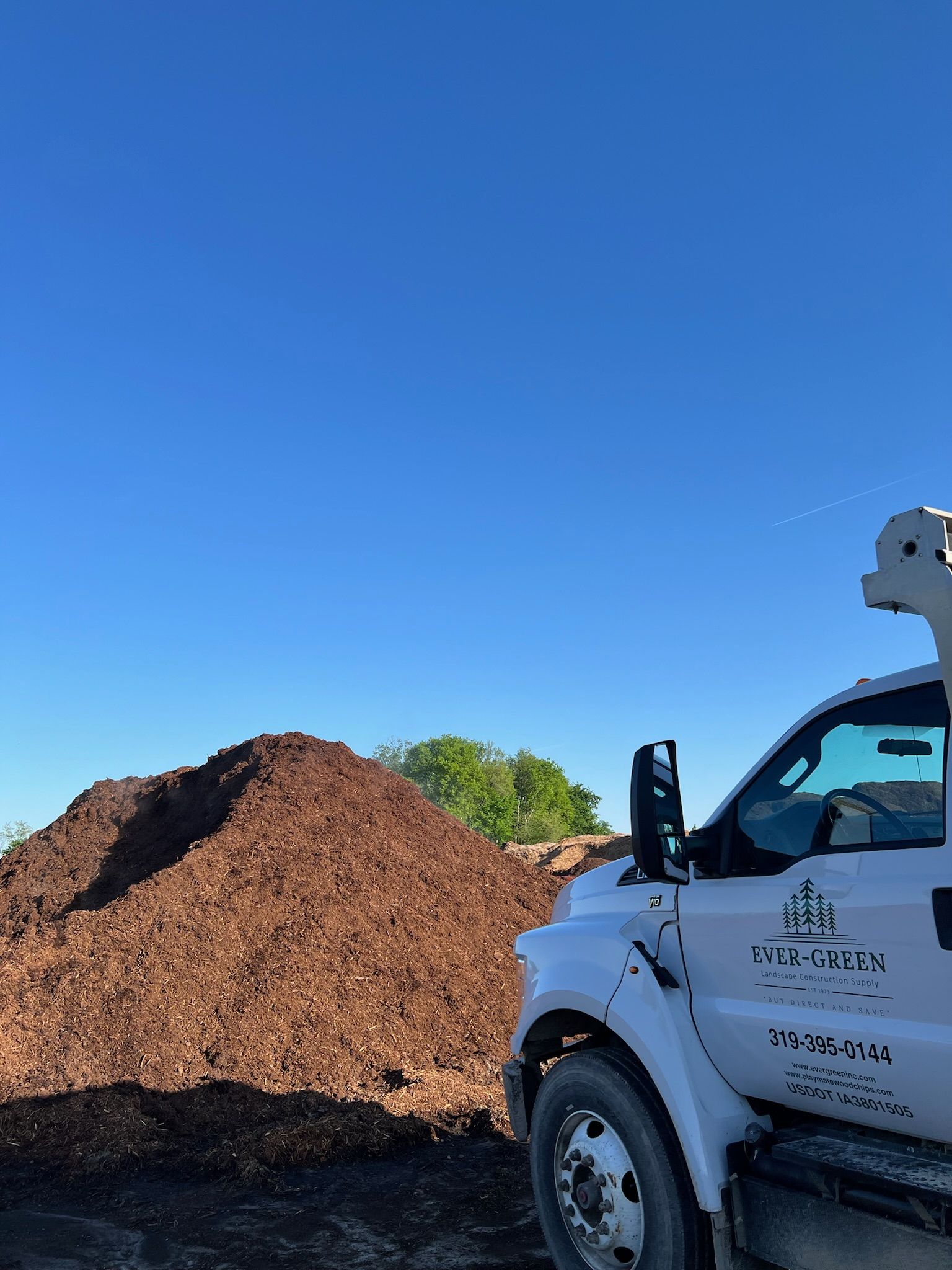 A large pile of mulch next to a white landscaping truck on a clear, blue-sky day.