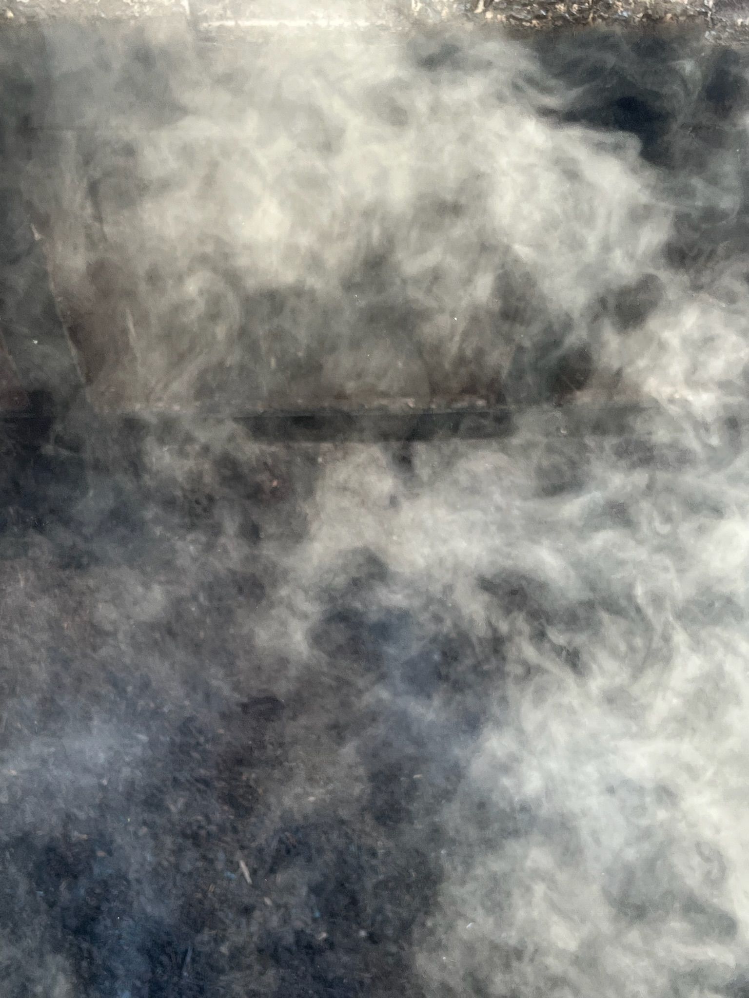 White smoke billowing over a dark, textured surface, creating a hazy, undefined cloud-like effect.