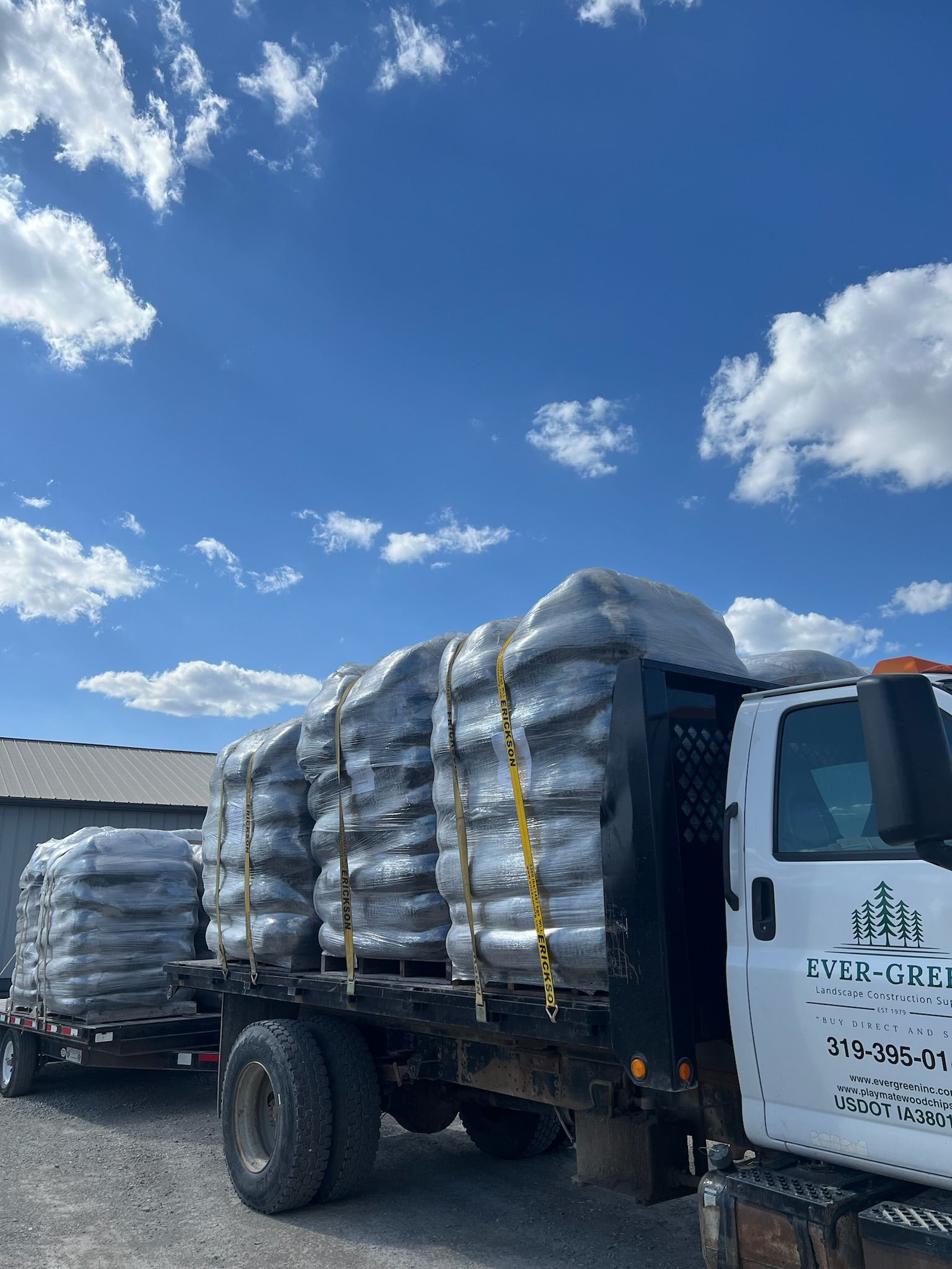 Truck carrying wrapped bags, under a partly cloudy blue sky.