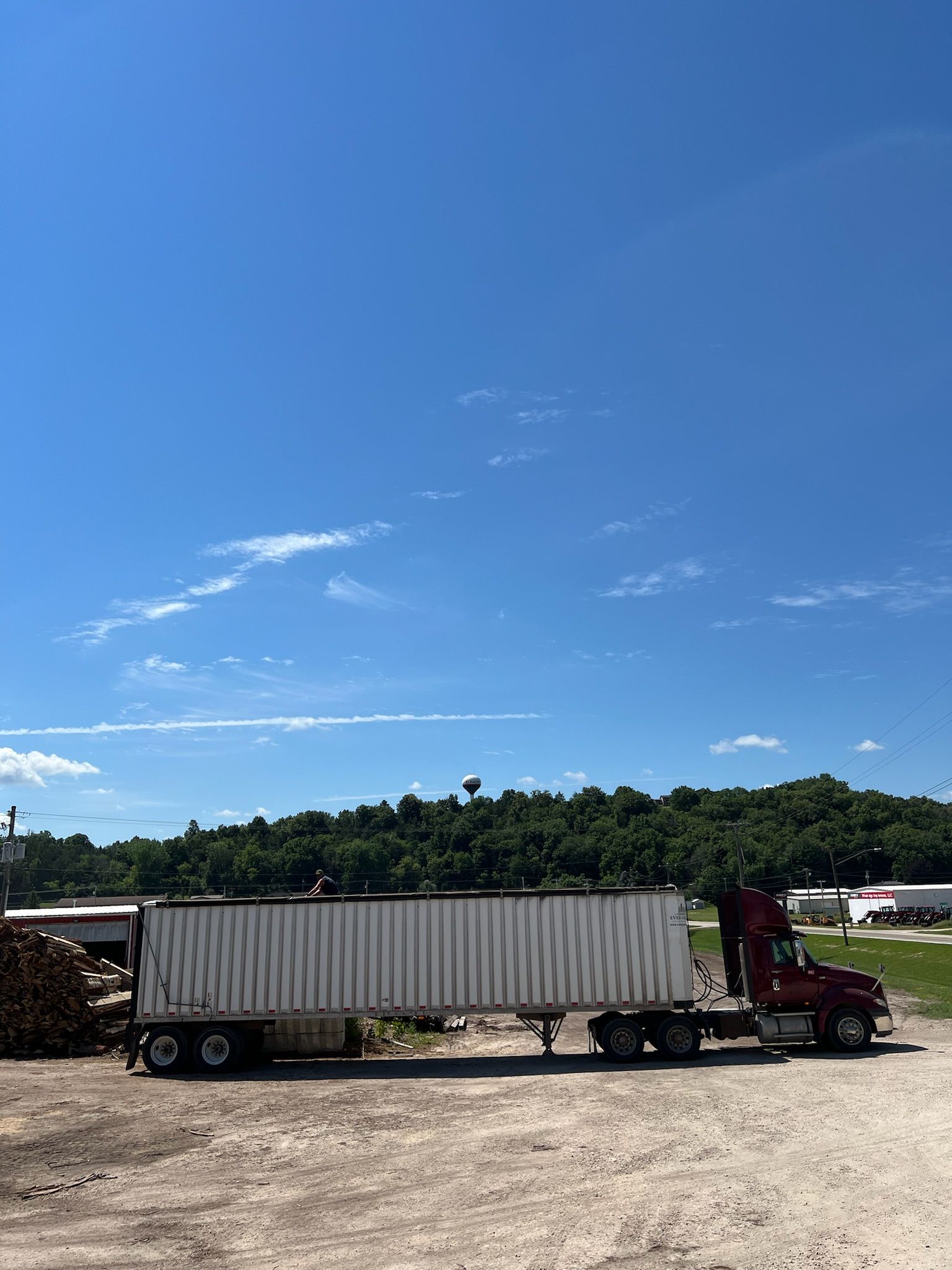 Red semi-truck with a white container on a gravel lot under a bright blue sky.