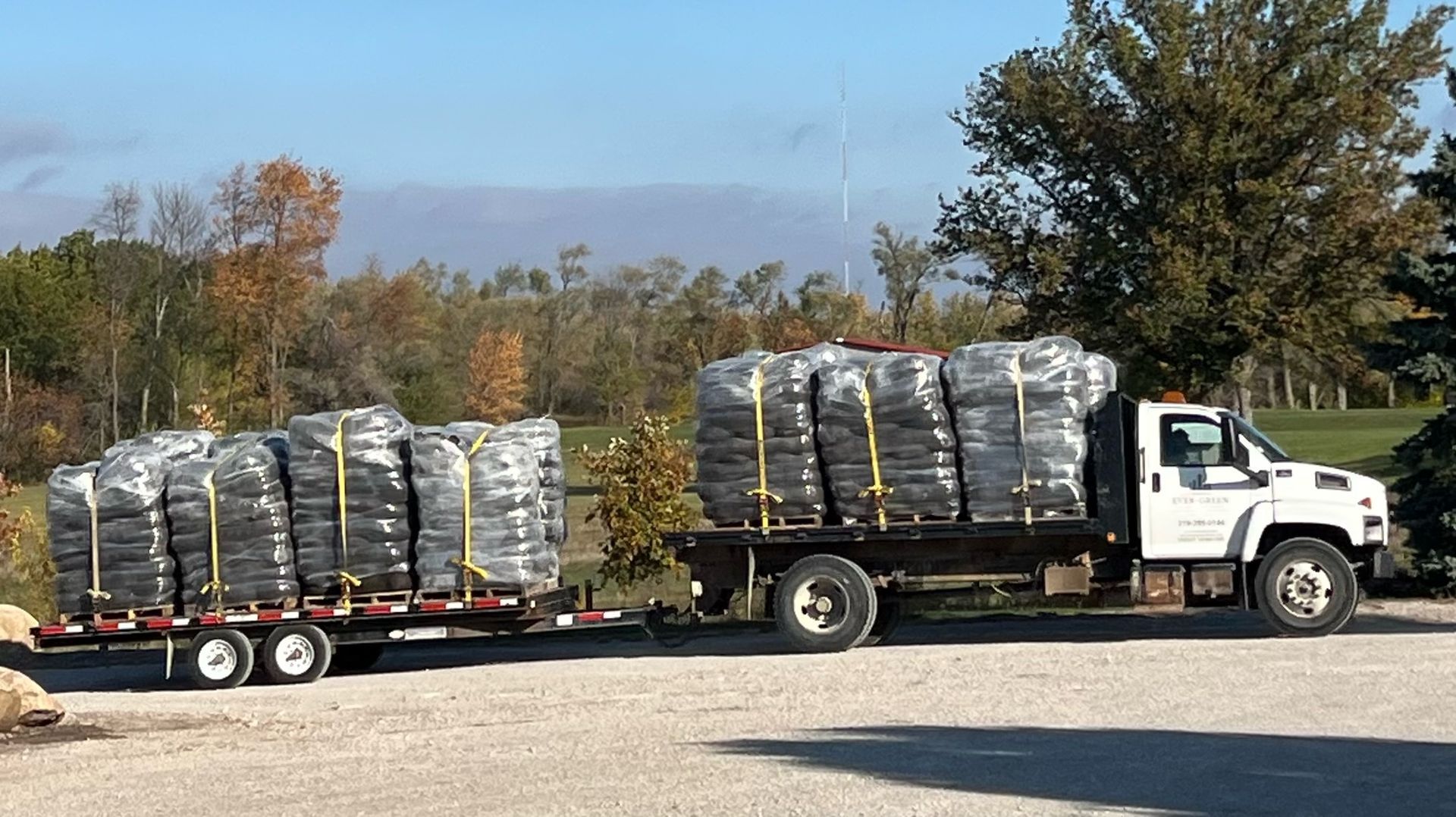 Truck and trailer loaded with numerous black bags, parked outdoors.
