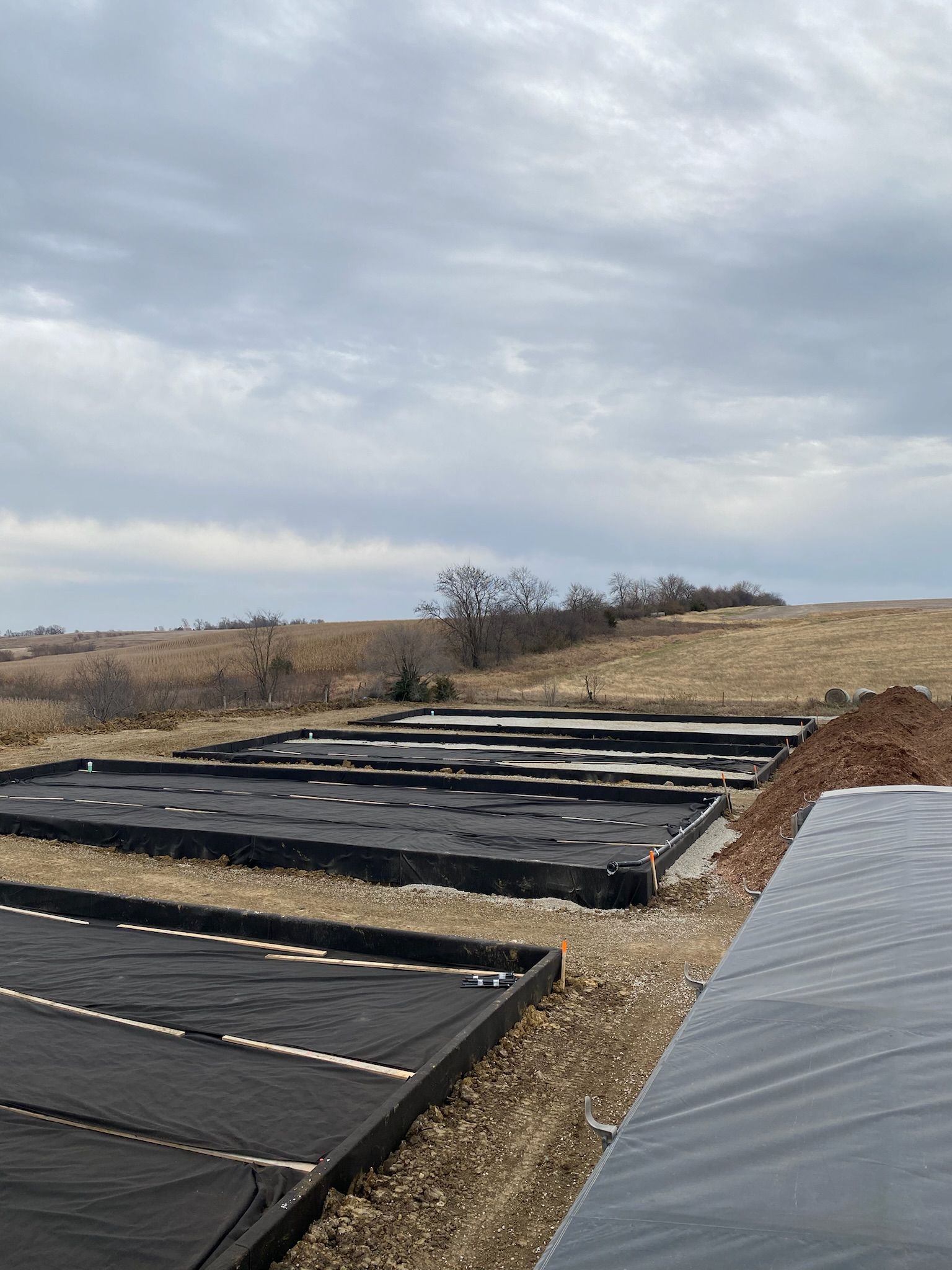 Black fabric covers rectangular plots in a field under a cloudy sky.