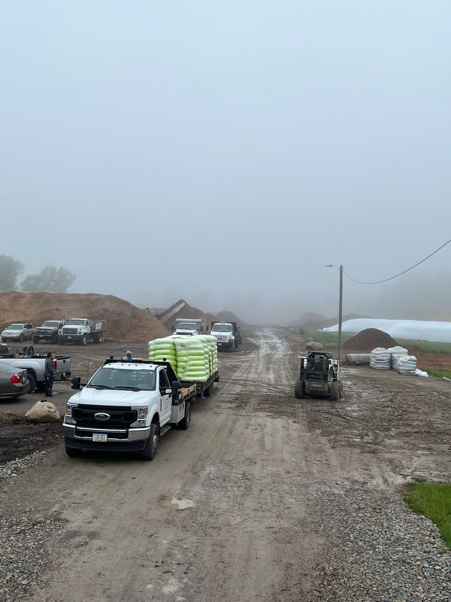 Trucks hauling supplies on a muddy construction site under a foggy sky.