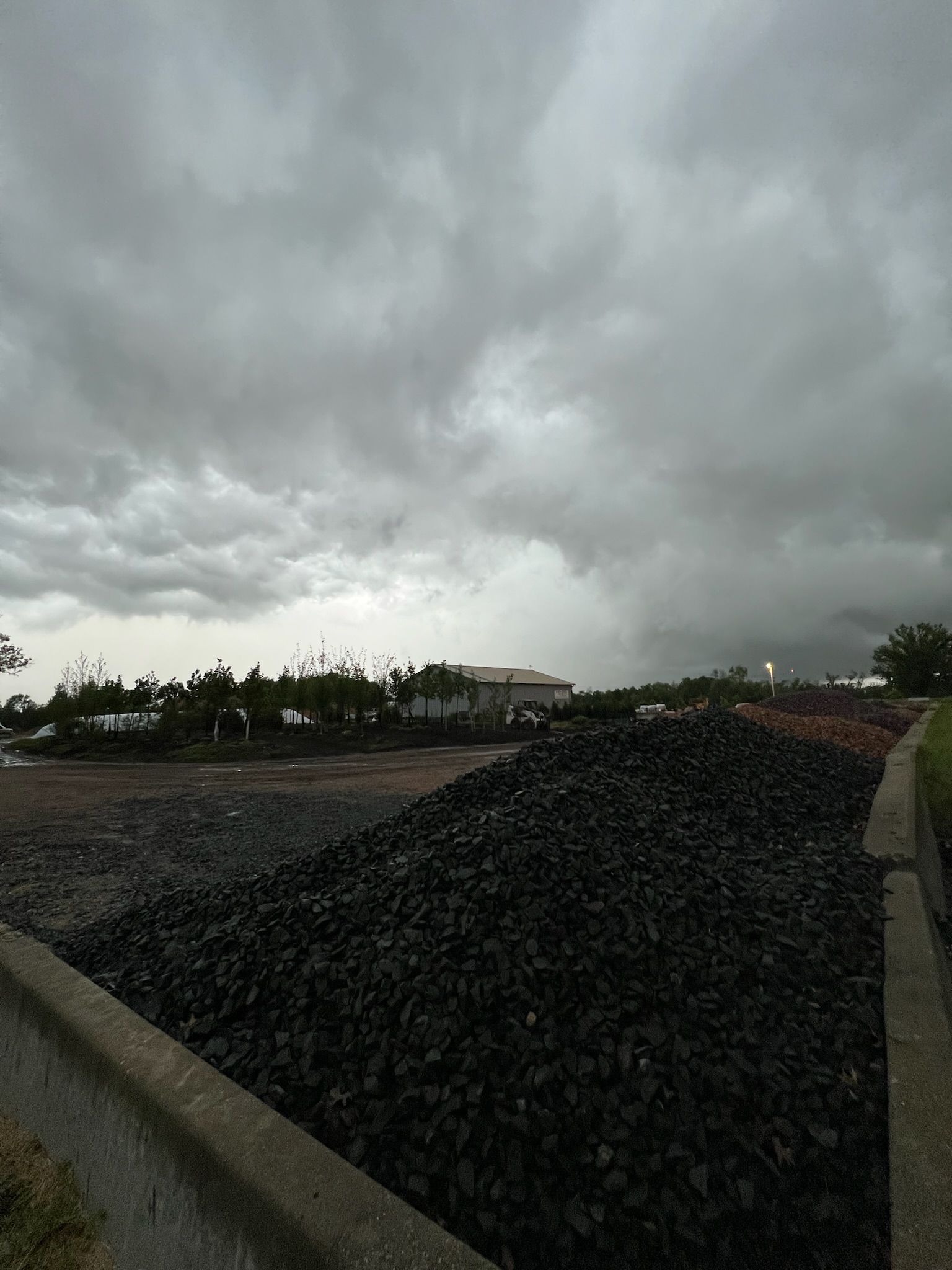 Dark cloudy sky over a pile of black material, possibly coal or rock, near a structure.