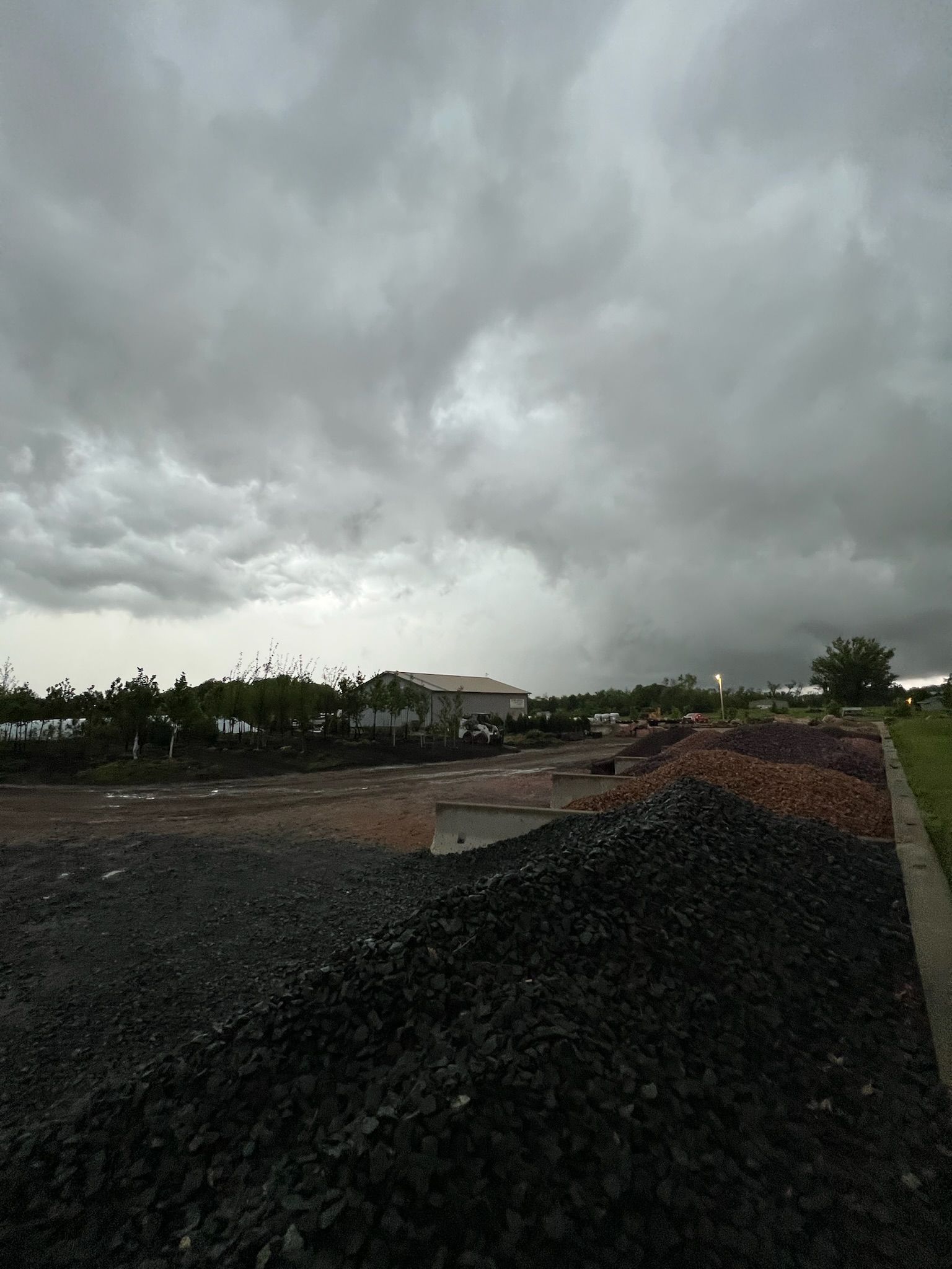 Overcast sky over a large outdoor area with piles of dark-colored material; a building is visible in the distance.
