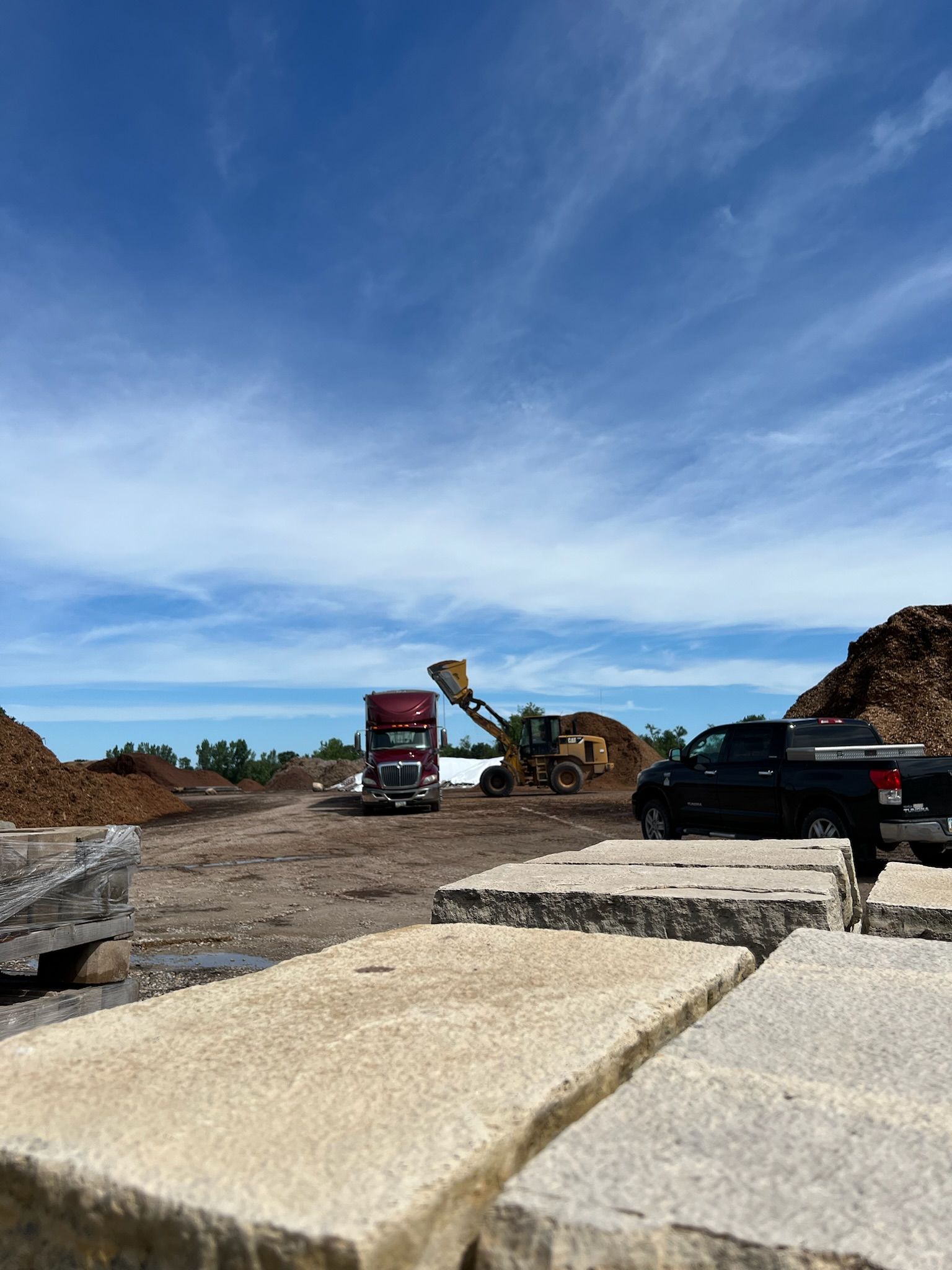 Construction site with machinery, a truck, and stacked stone blocks under a blue sky.
