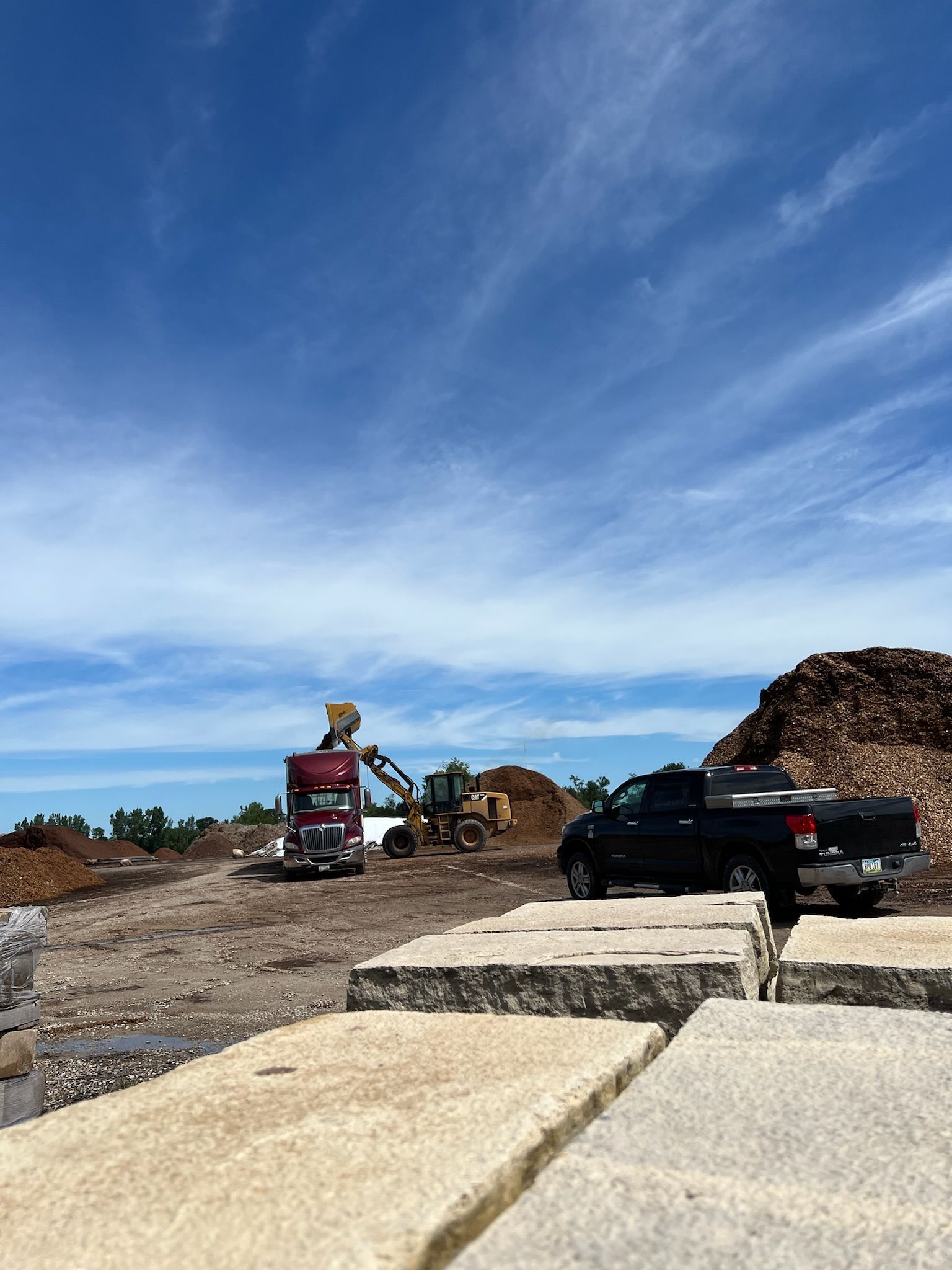 Construction site with machinery, including a truck, excavator, and pickup truck, under a blue sky.