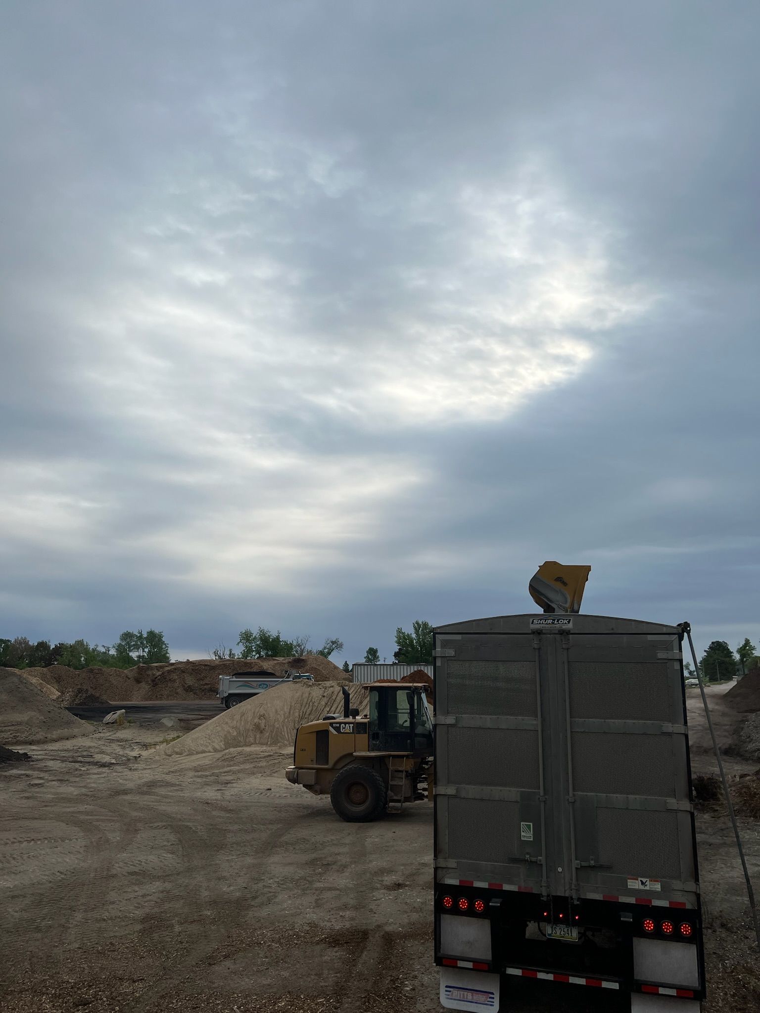 Construction site with a truck and loader under a cloudy sky.