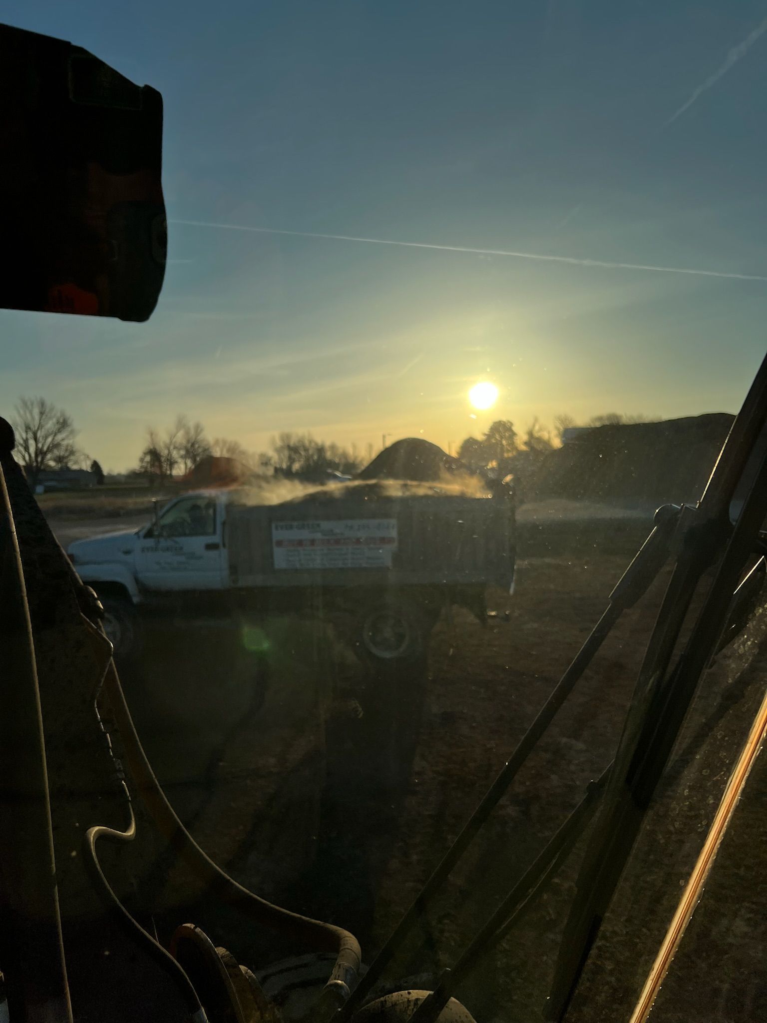 Bright sun shines over a white pickup truck loaded with material, seen from machinery cab.