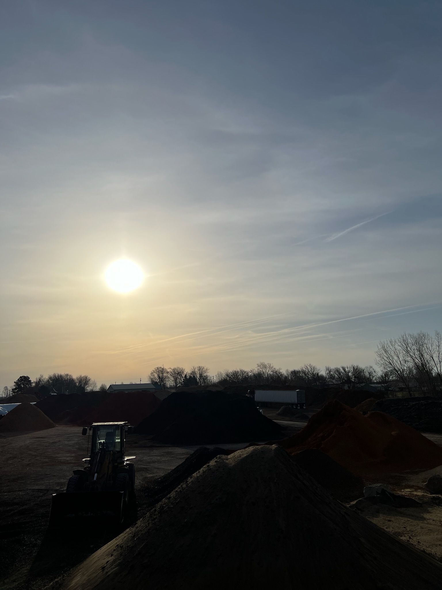 Sunlit construction site, piles of materials, and a loader under a hazy sky.