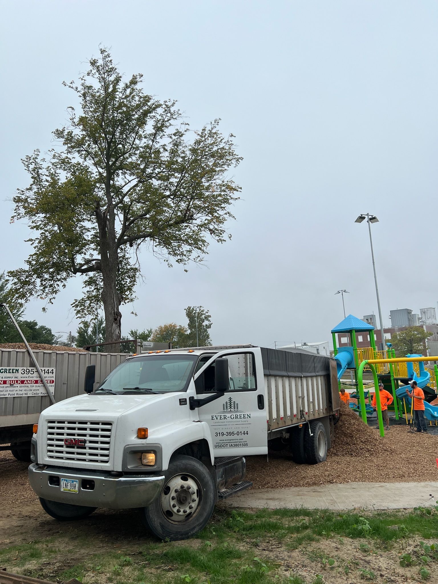 White truck dumping mulch at a playground.