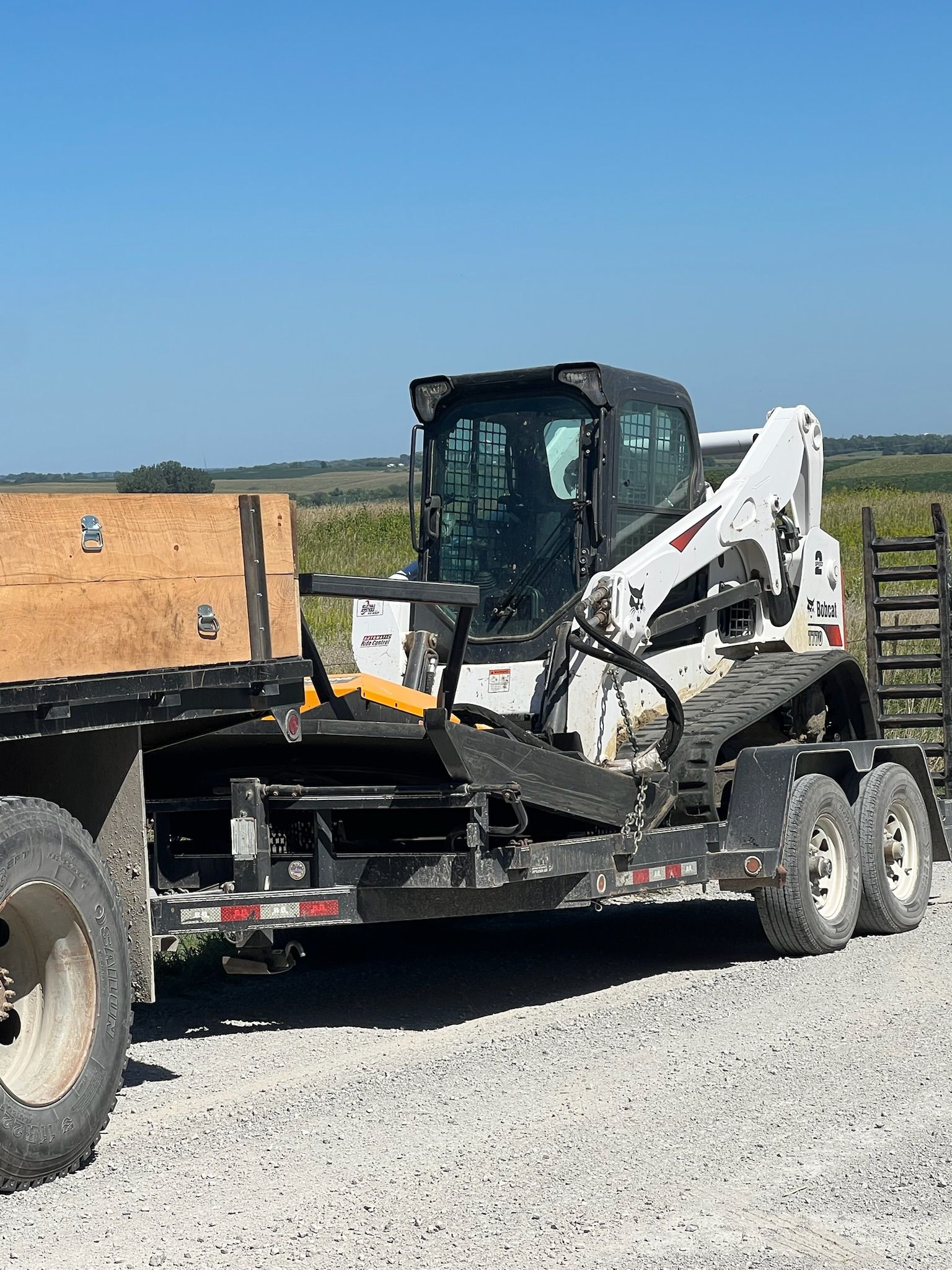 Bobcat skid-steer loader on a trailer in an outdoor setting with a blue sky.