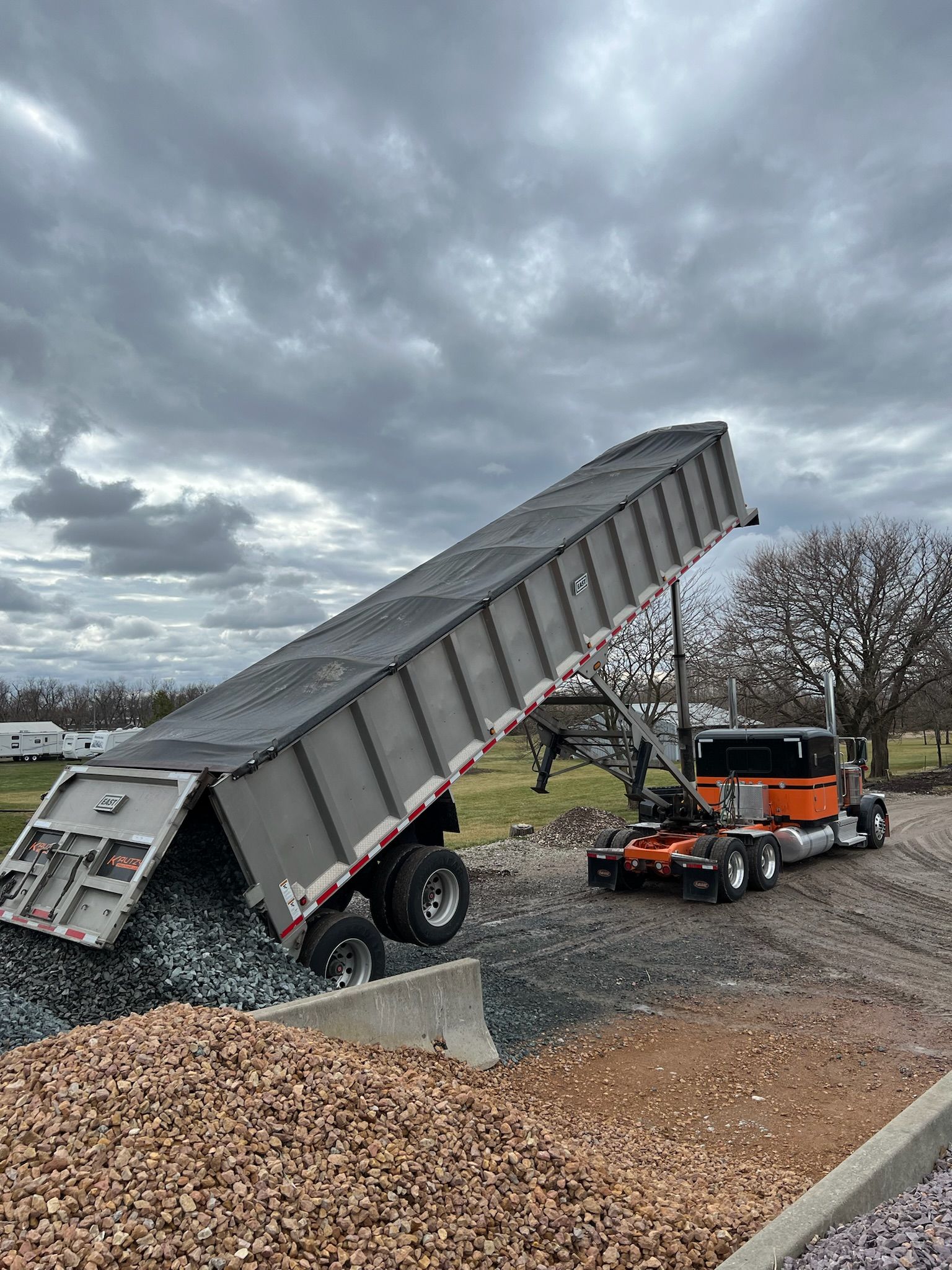 A dump truck unloading gravel on a construction site under a cloudy sky.