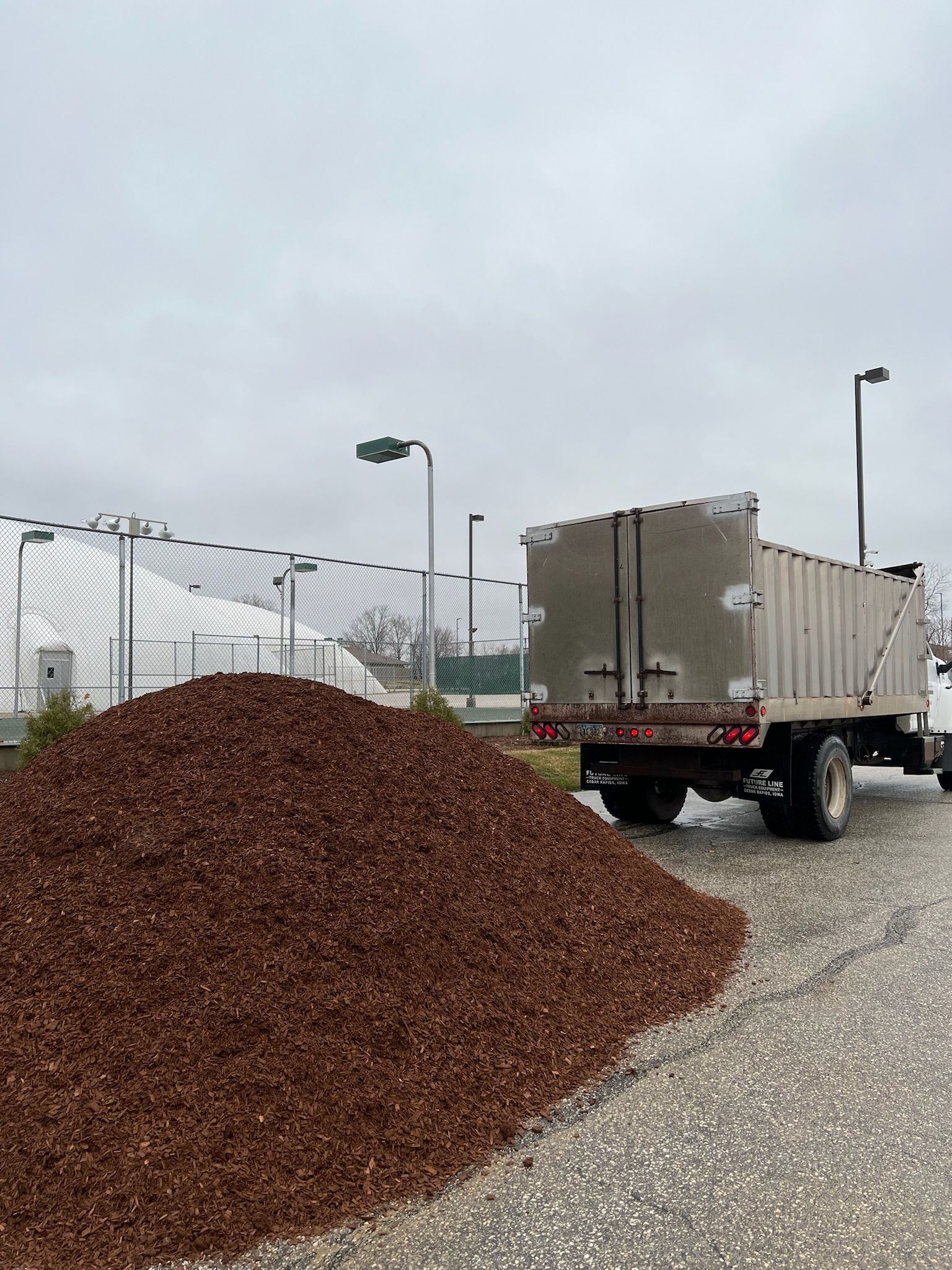 A large pile of brown mulch next to a truck. Truck bed is open; a cloudy day.