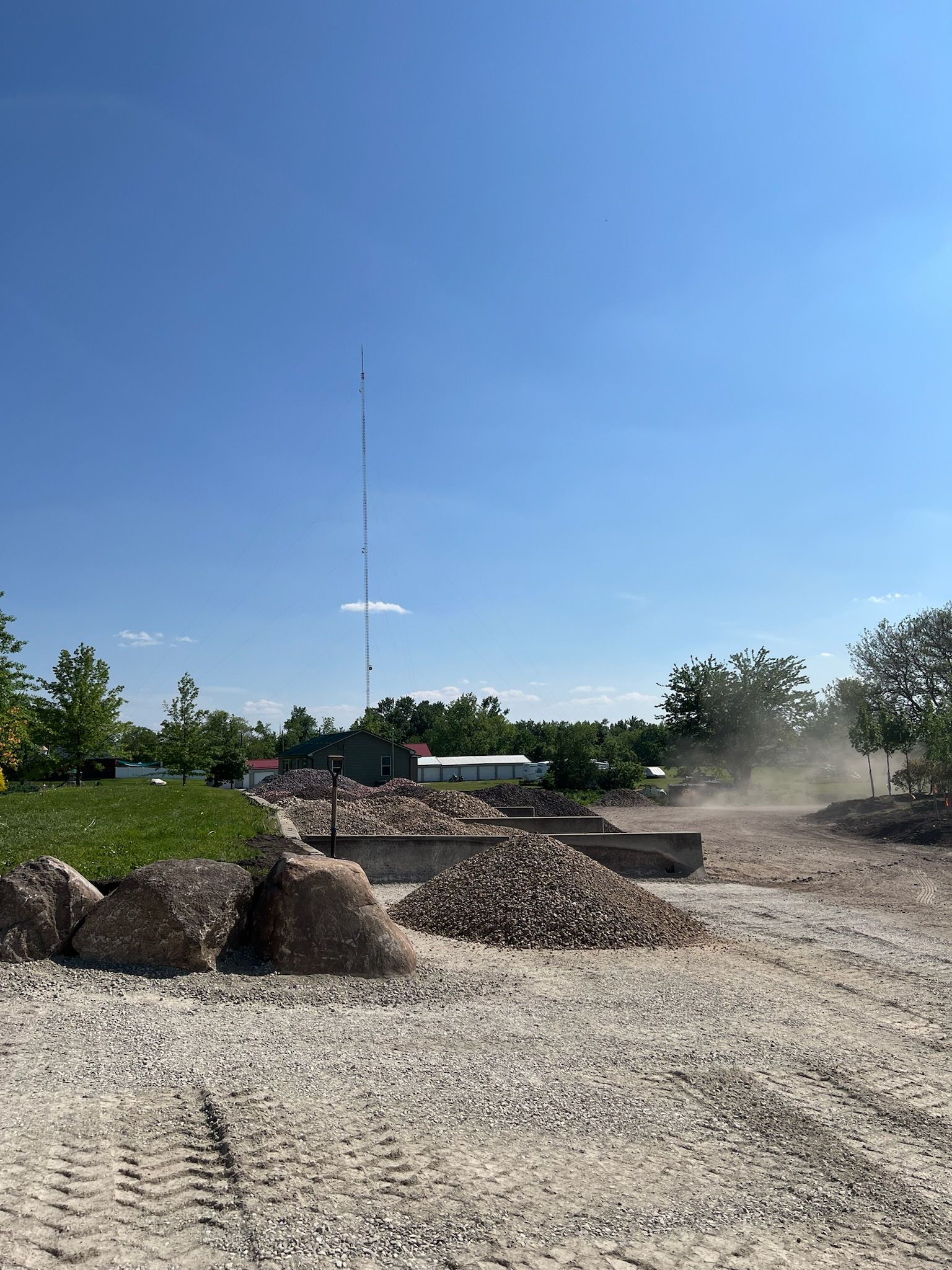 Construction site with piles of gravel, a tall communication tower, and blue sky.
