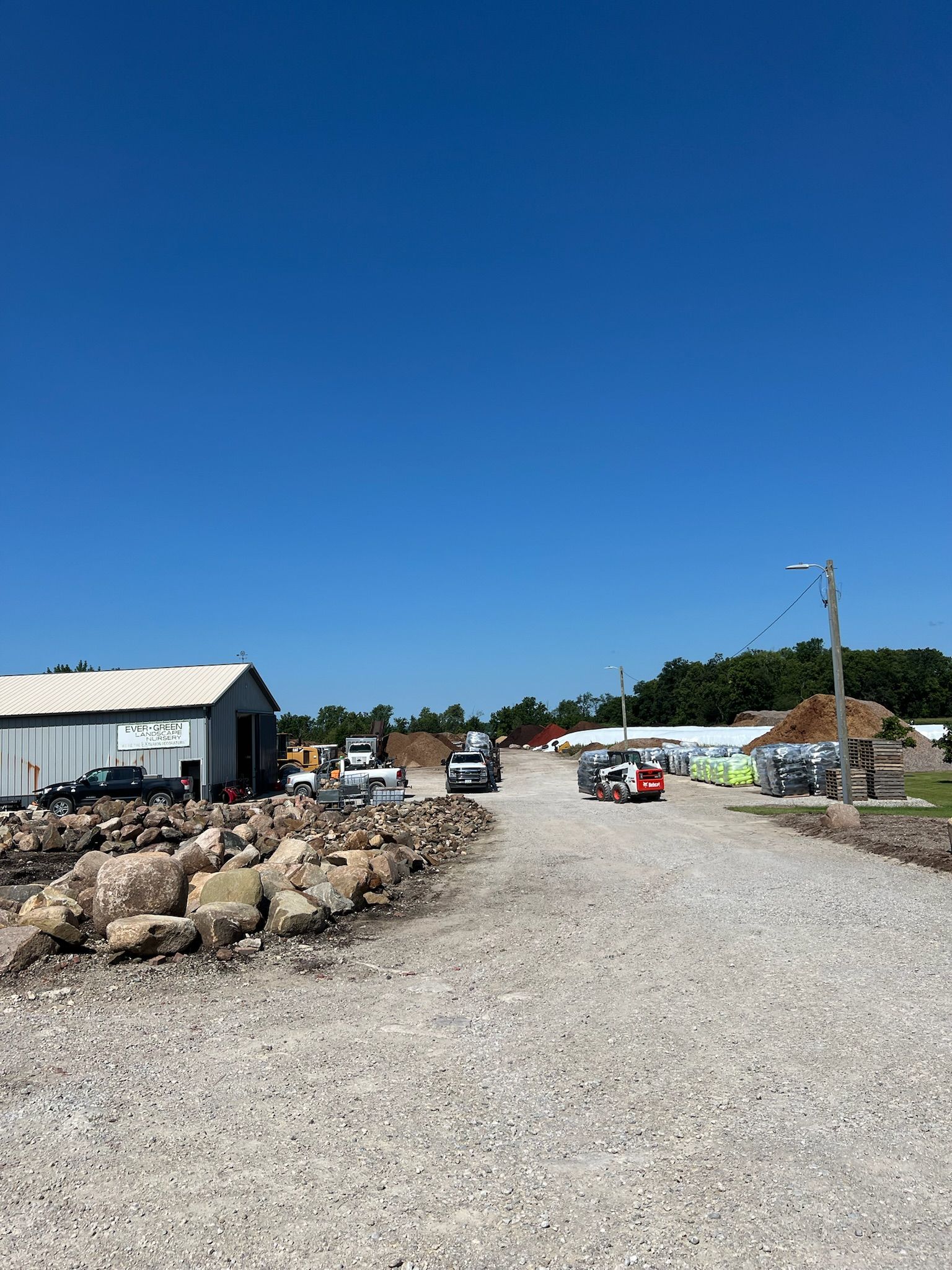 Gravel road leads to buildings and vehicles on a sunny day with a clear blue sky.