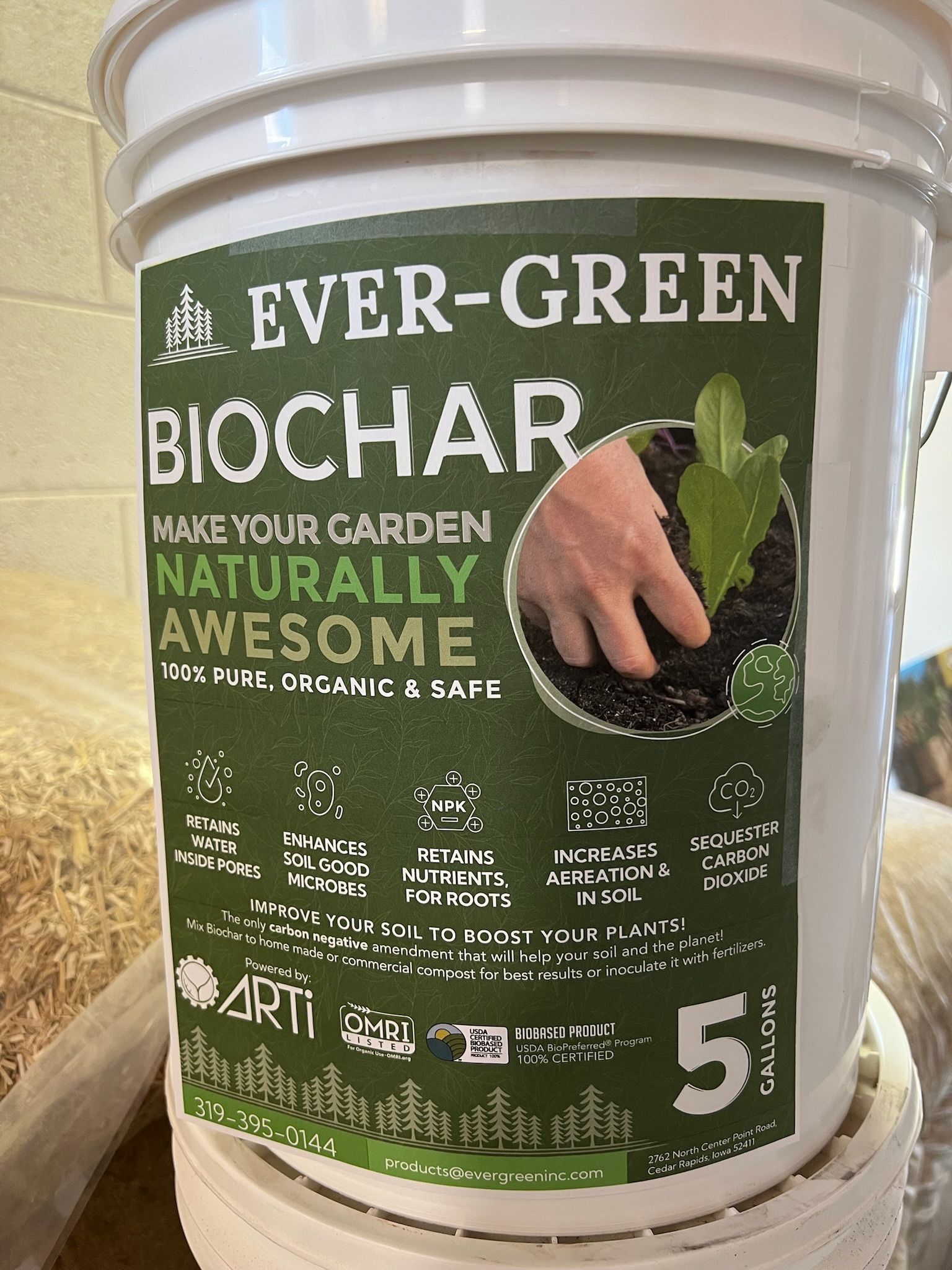 White bucket of Evergreen Biochar, with a hand planting a seedling in the soil, green and white label.
