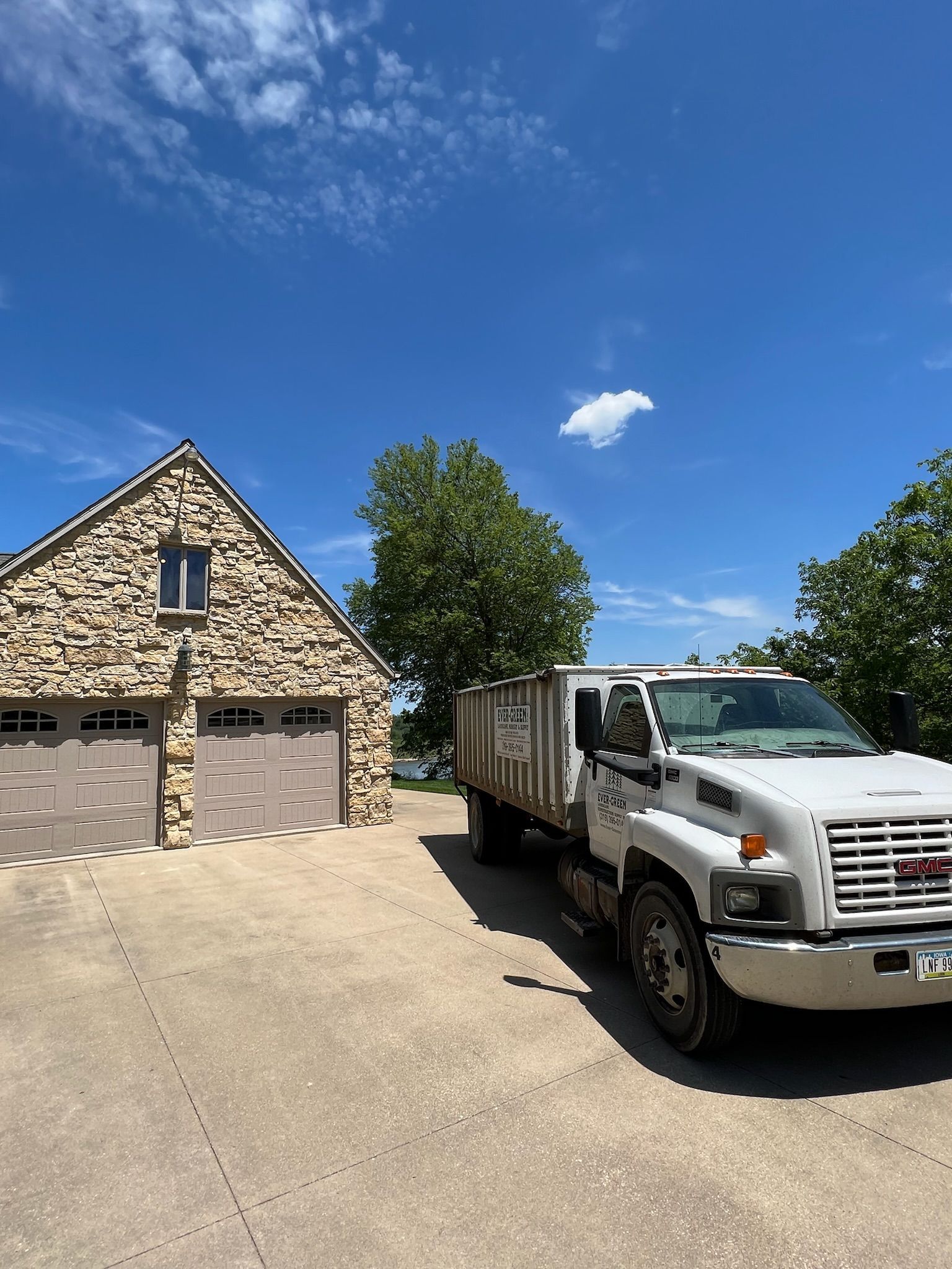 White dump truck parked in driveway next to stone garage on a sunny day.