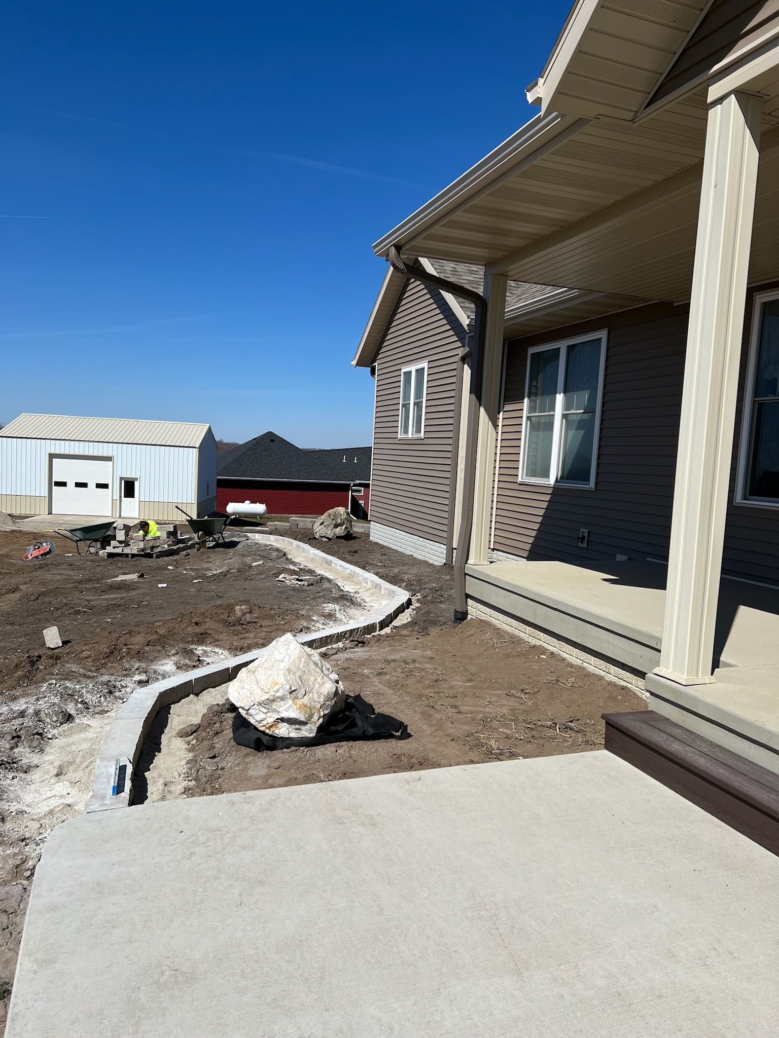 House exterior with porch, concrete pathway, and trench; blue sky in the background.
