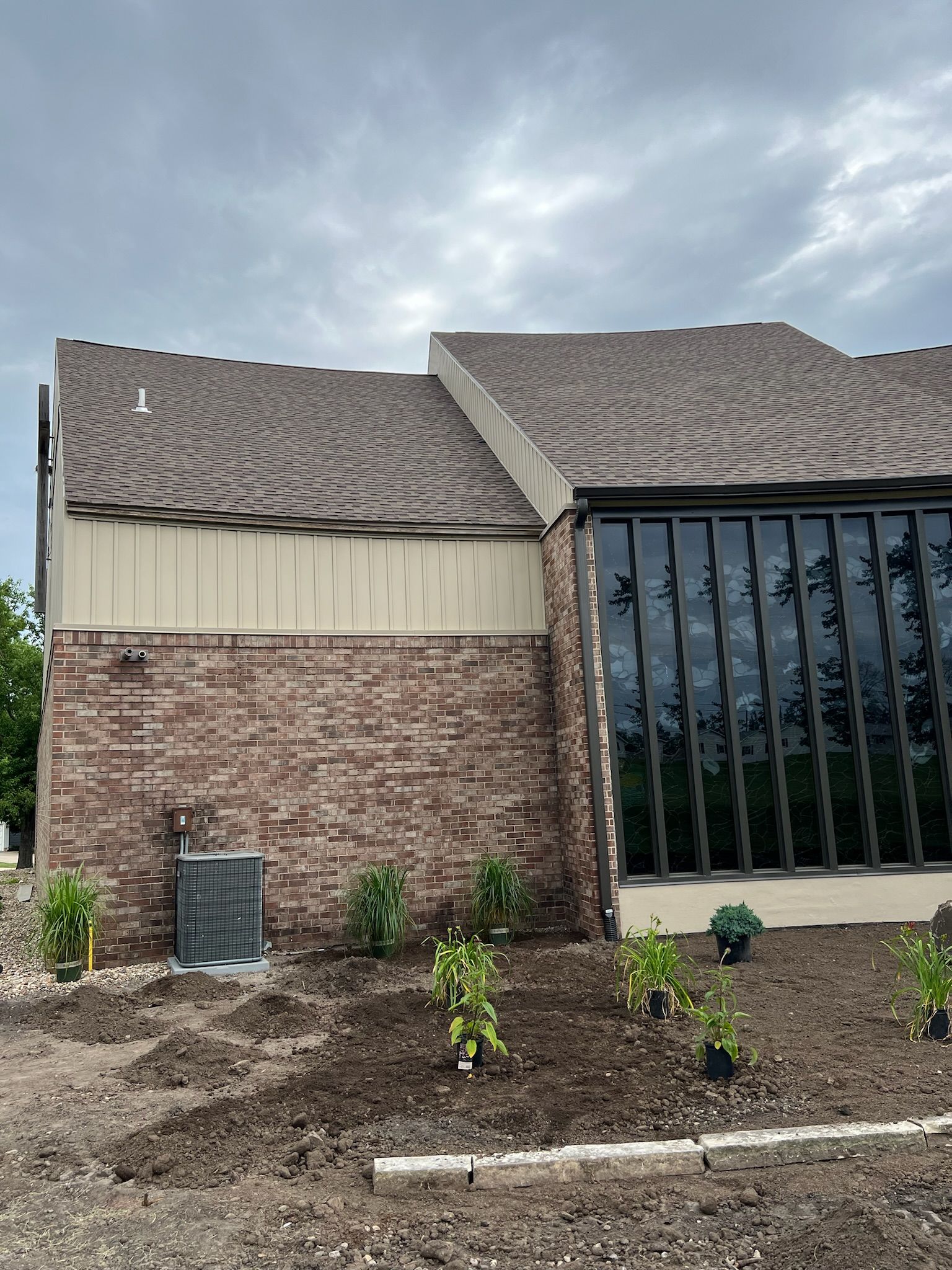 Side of a building with brick and large windows, brown roof, and new landscaping.