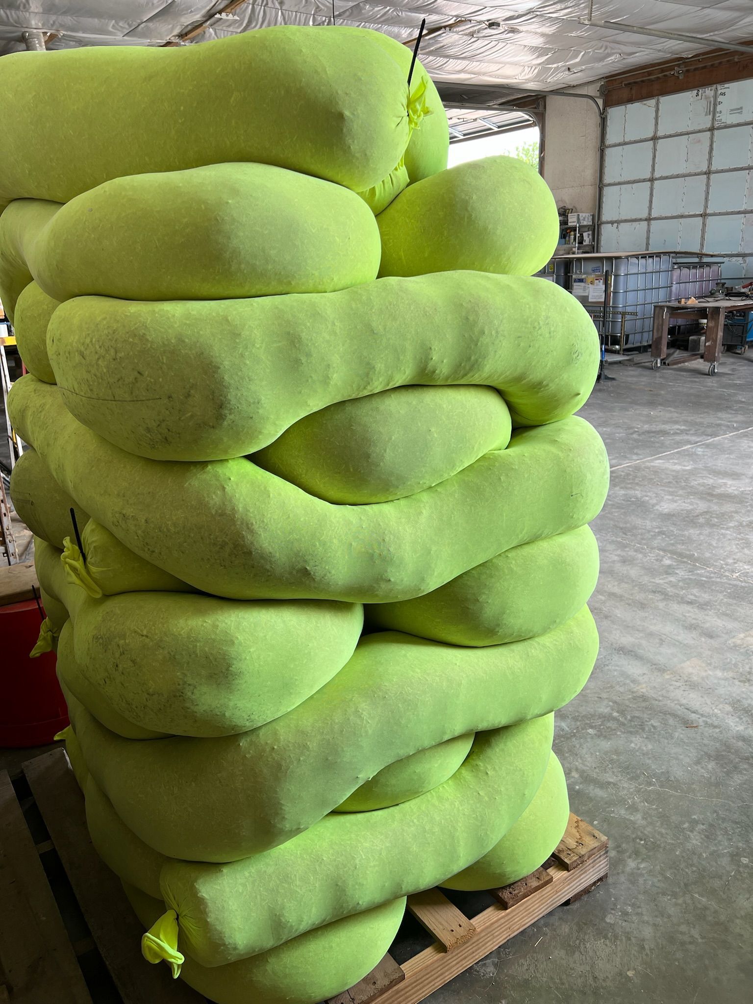 Stack of lime green cylindrical absorbent booms on a wooden pallet in a warehouse.