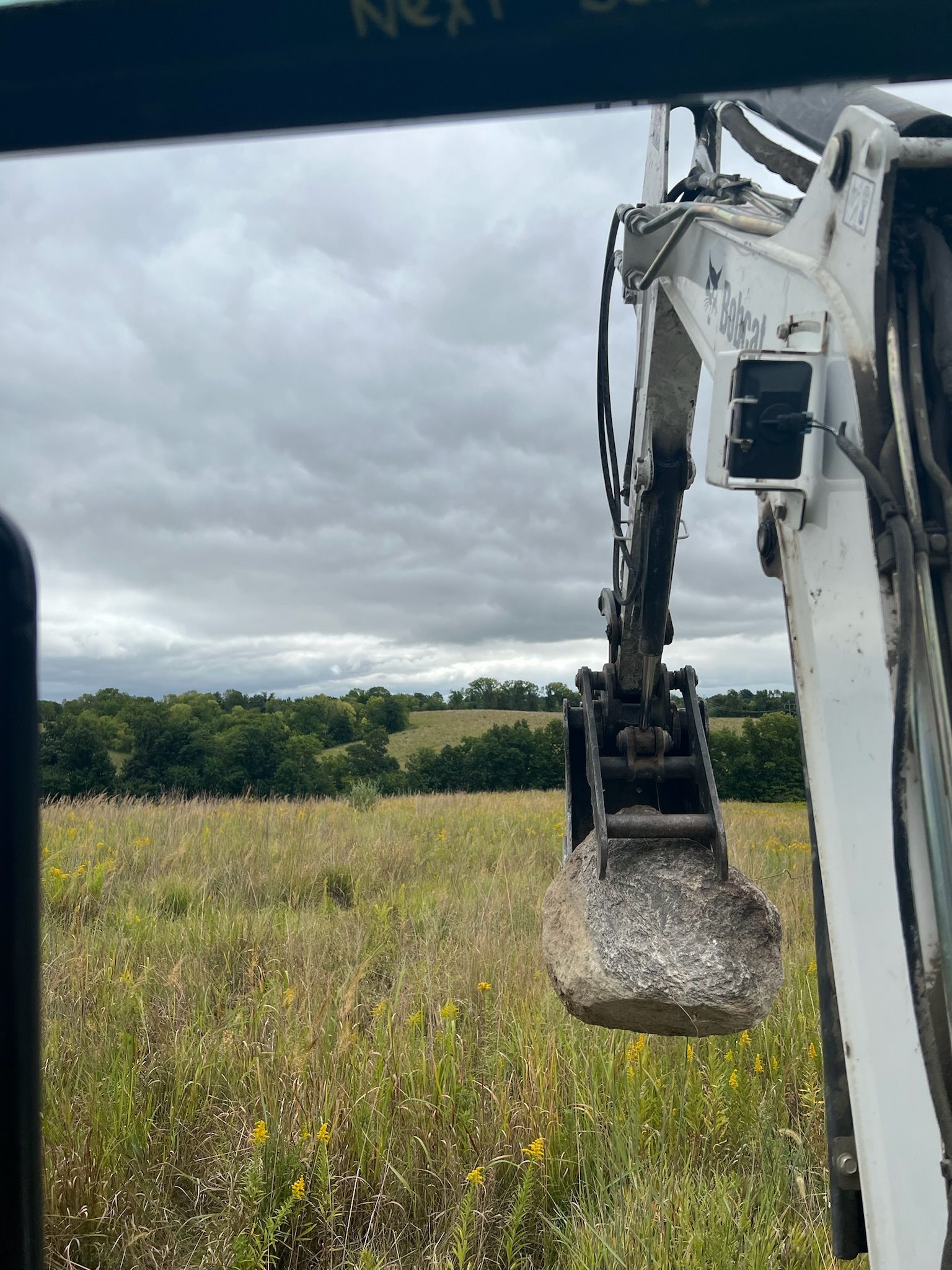 An excavator bucket in a field, under cloudy skies.