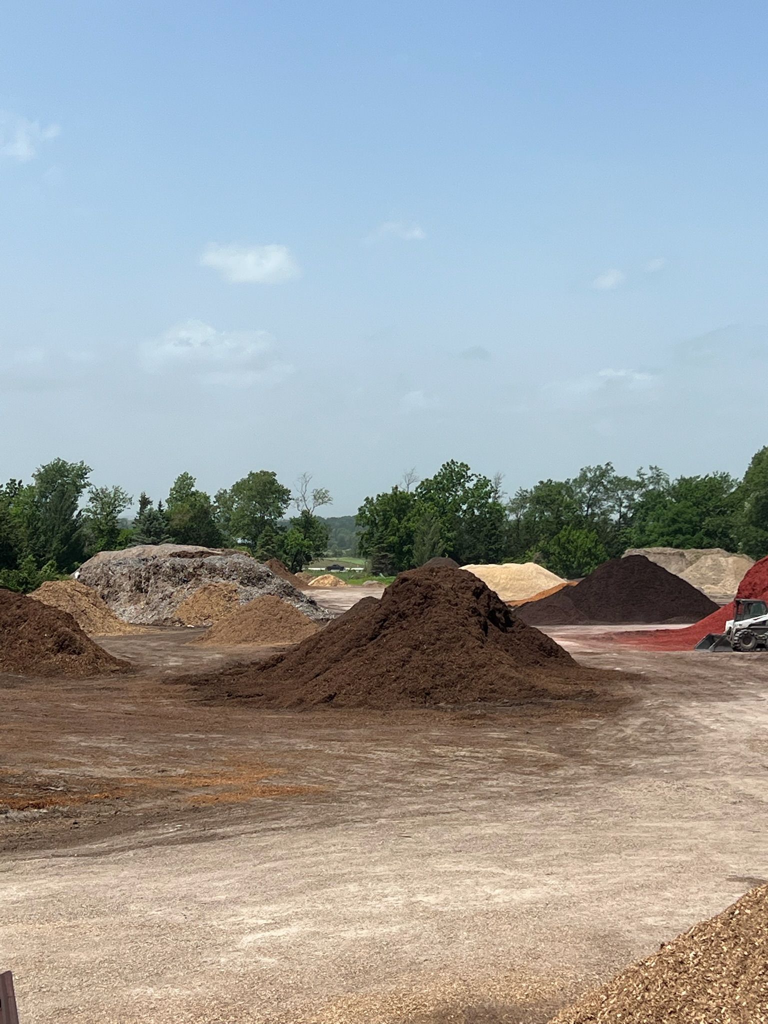 Mulch piles in an outdoor setting under a partly cloudy sky.