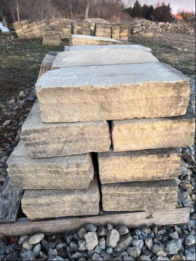Stack of light-colored rectangular stone blocks on a wooden pallet, outdoors on gravel.