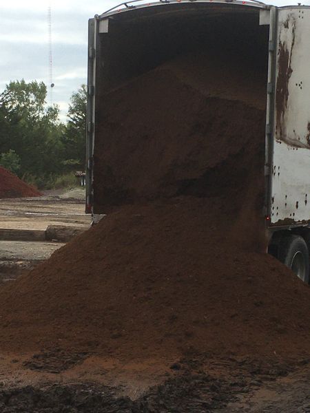Brown mulch spilling from a white truck bed onto a paved area, trees in the background.