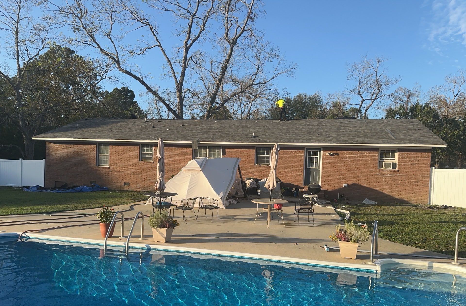 Brick house with pool in backyard; person on roof, patio furniture, tent.