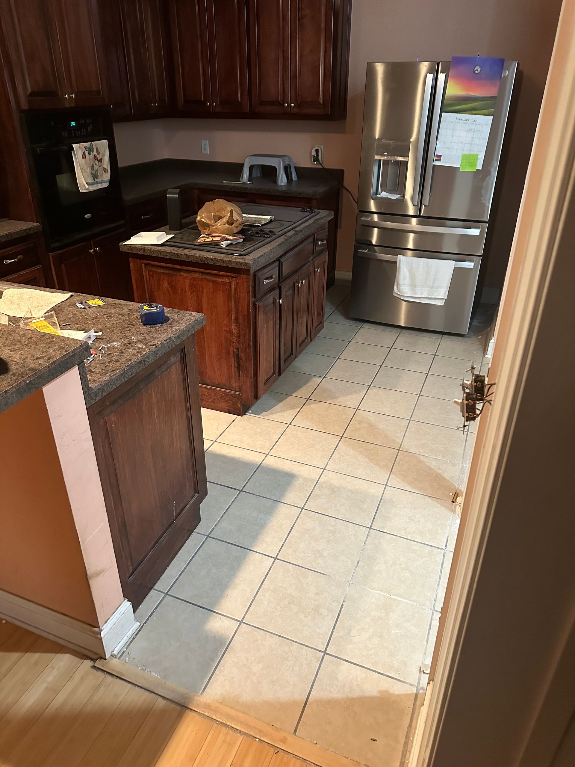 Kitchen with dark wood cabinets, island, and stainless steel refrigerator on tiled floor.