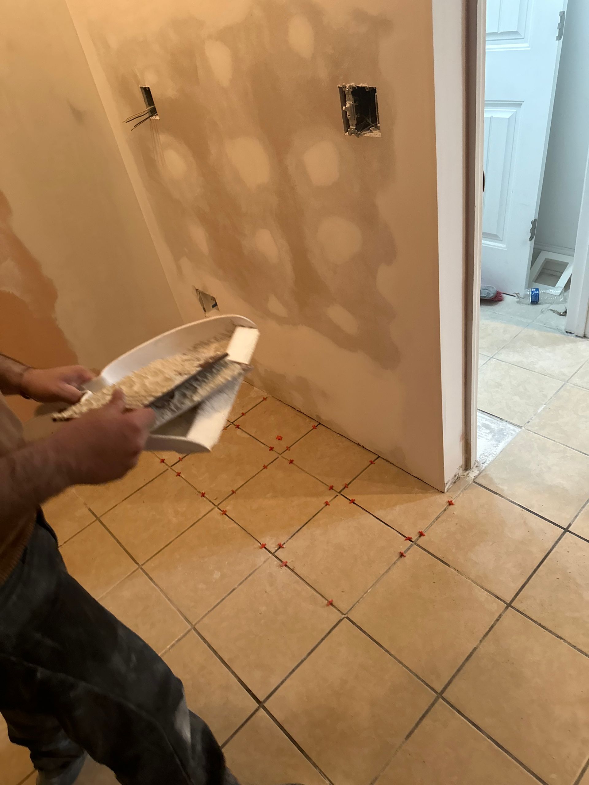 Person spreading grout between tiles on a kitchen floor; wall and door in background.