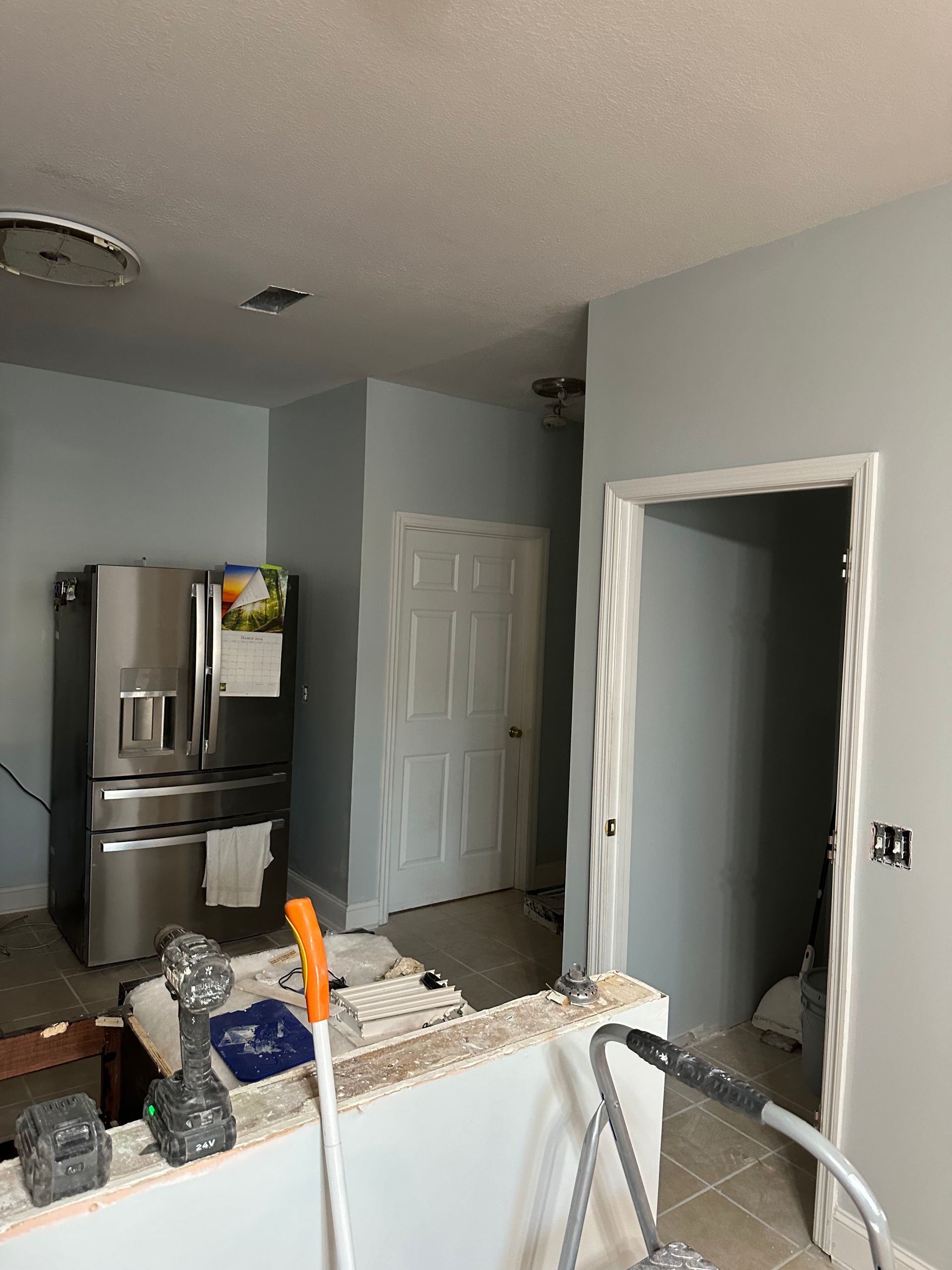 Kitchen interior with refrigerator, door, and half wall being renovated; walls painted light blue.