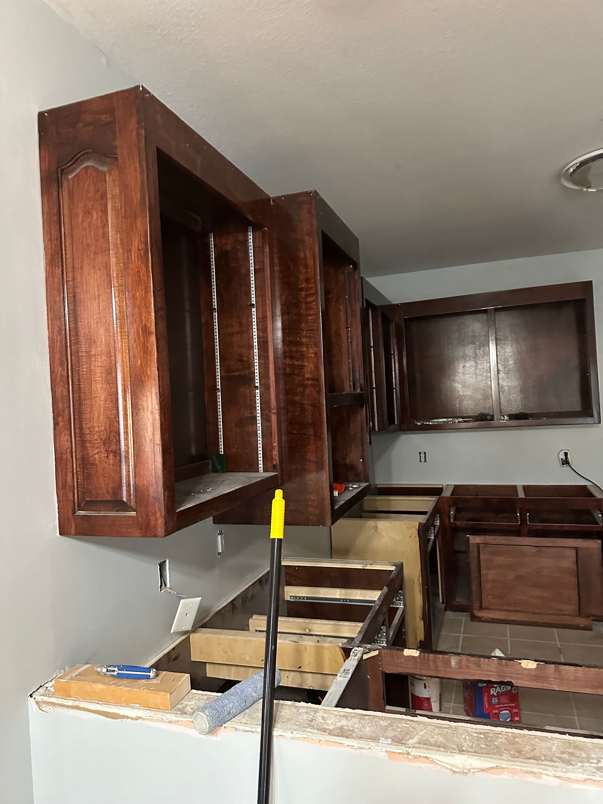 Kitchen cabinets, unfinished remodel. Dark stained wood cabinets mounted on gray walls. Construction in progress.