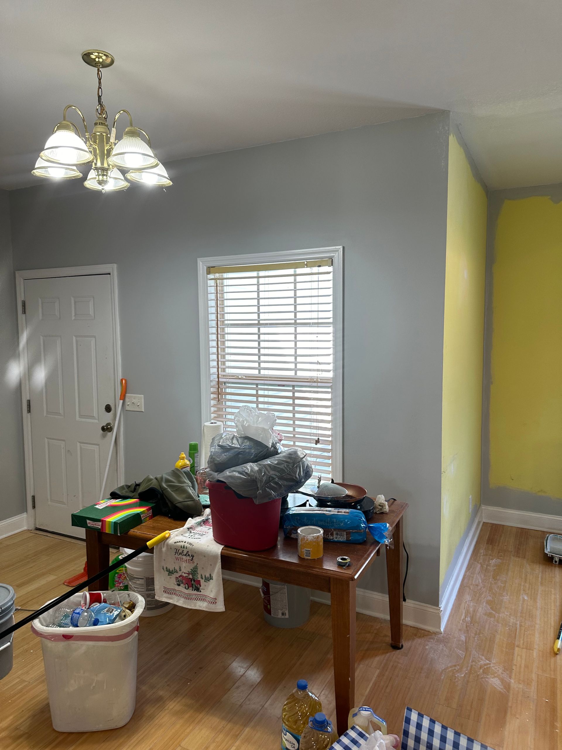 A room with a table cluttered with items, a window, a door, and gray and yellow walls.